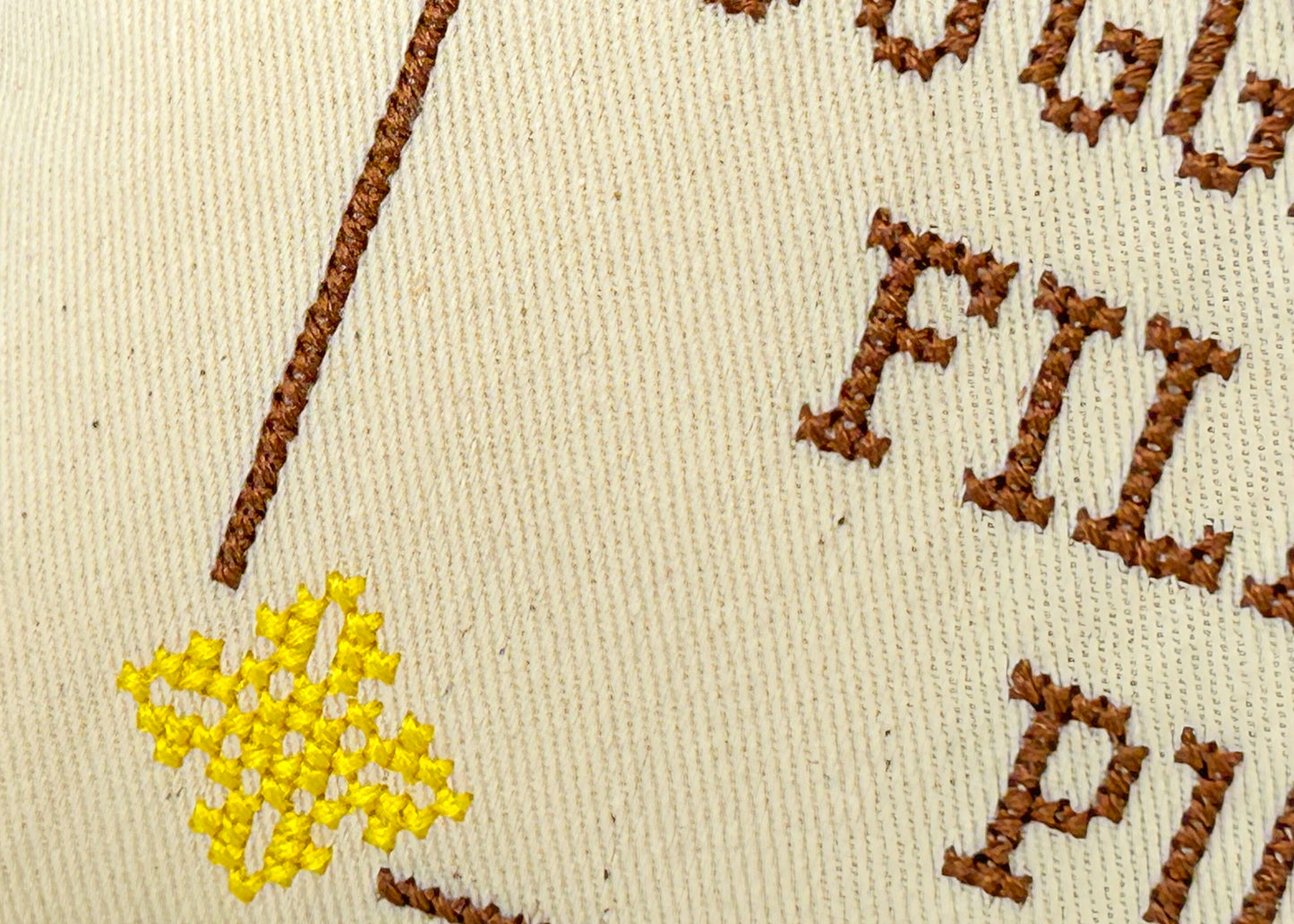 close up embroidery showing cross stitch on cream fabric. Brown and yellow embroidery thread.