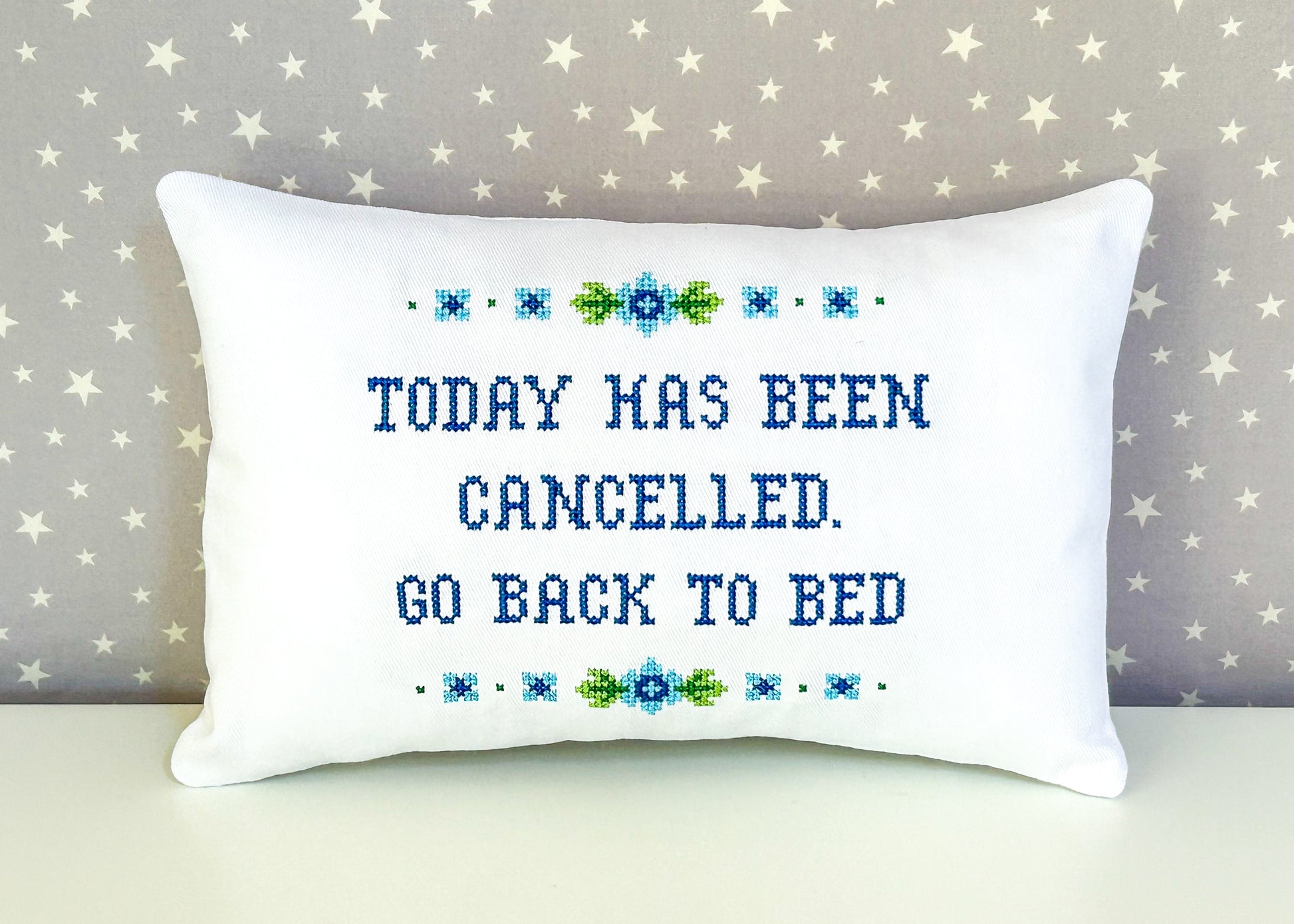 Decorative pillow with cross-stitched text on a star-patterned background