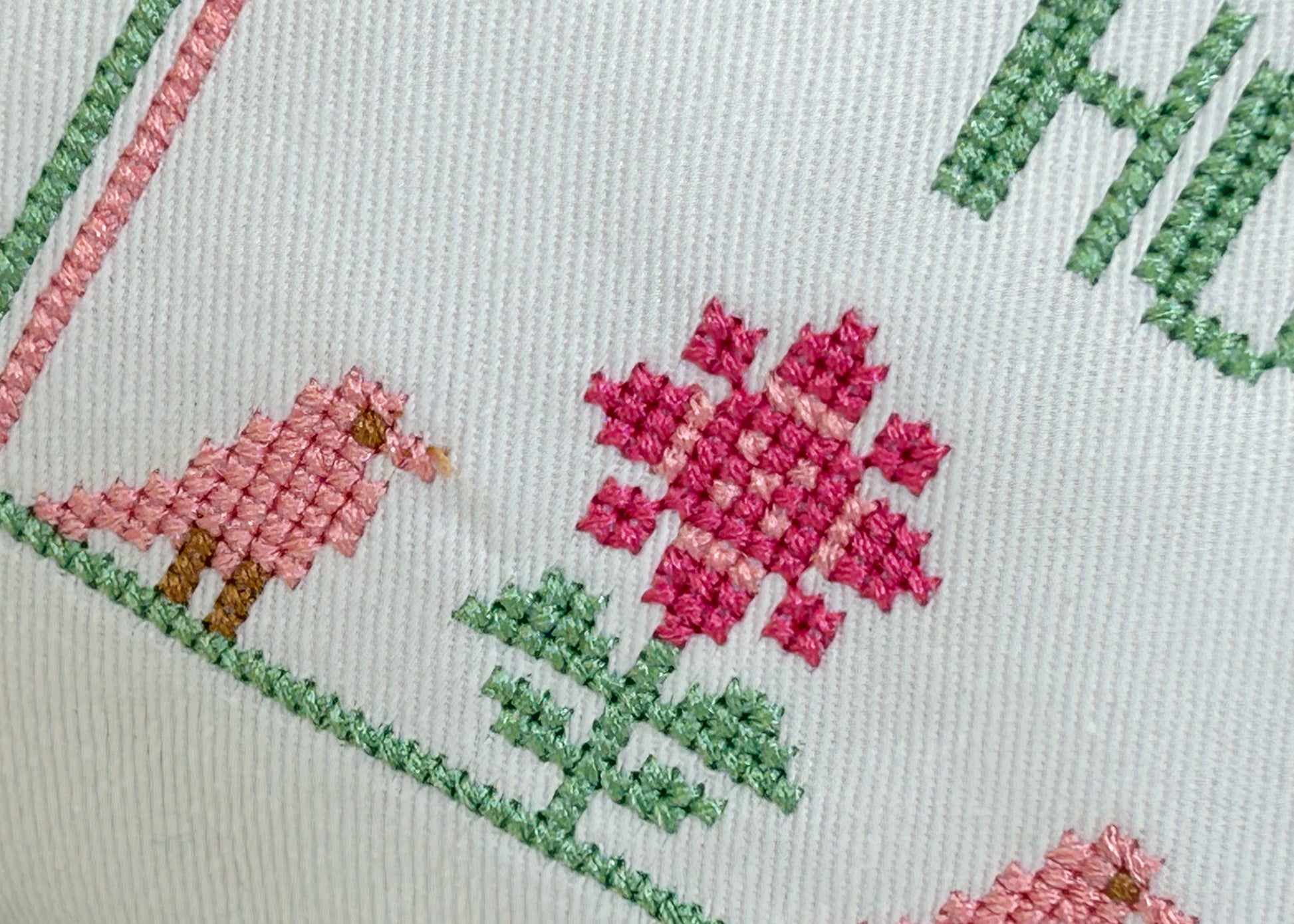 Close-up of cross-stitched design with pink flowers and green leaves on a light background