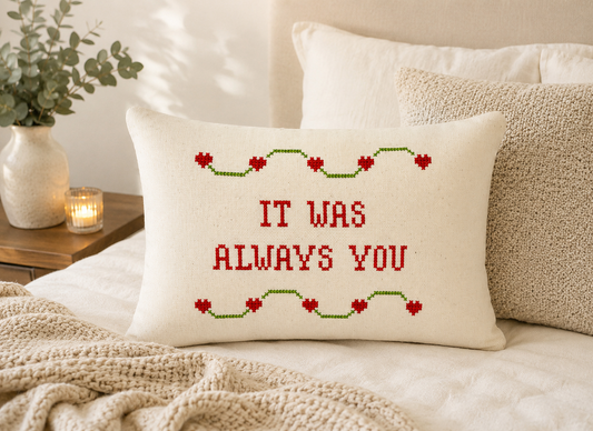 Decorative pillow with 'It was always you' text on a bed with a plant and candle in the background.
