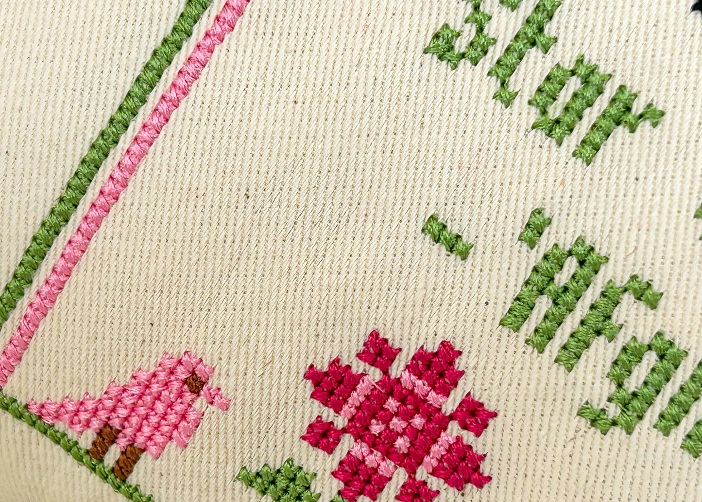 Close-up of cross-stitched design with pink flowers and green leaves on beige fabric.