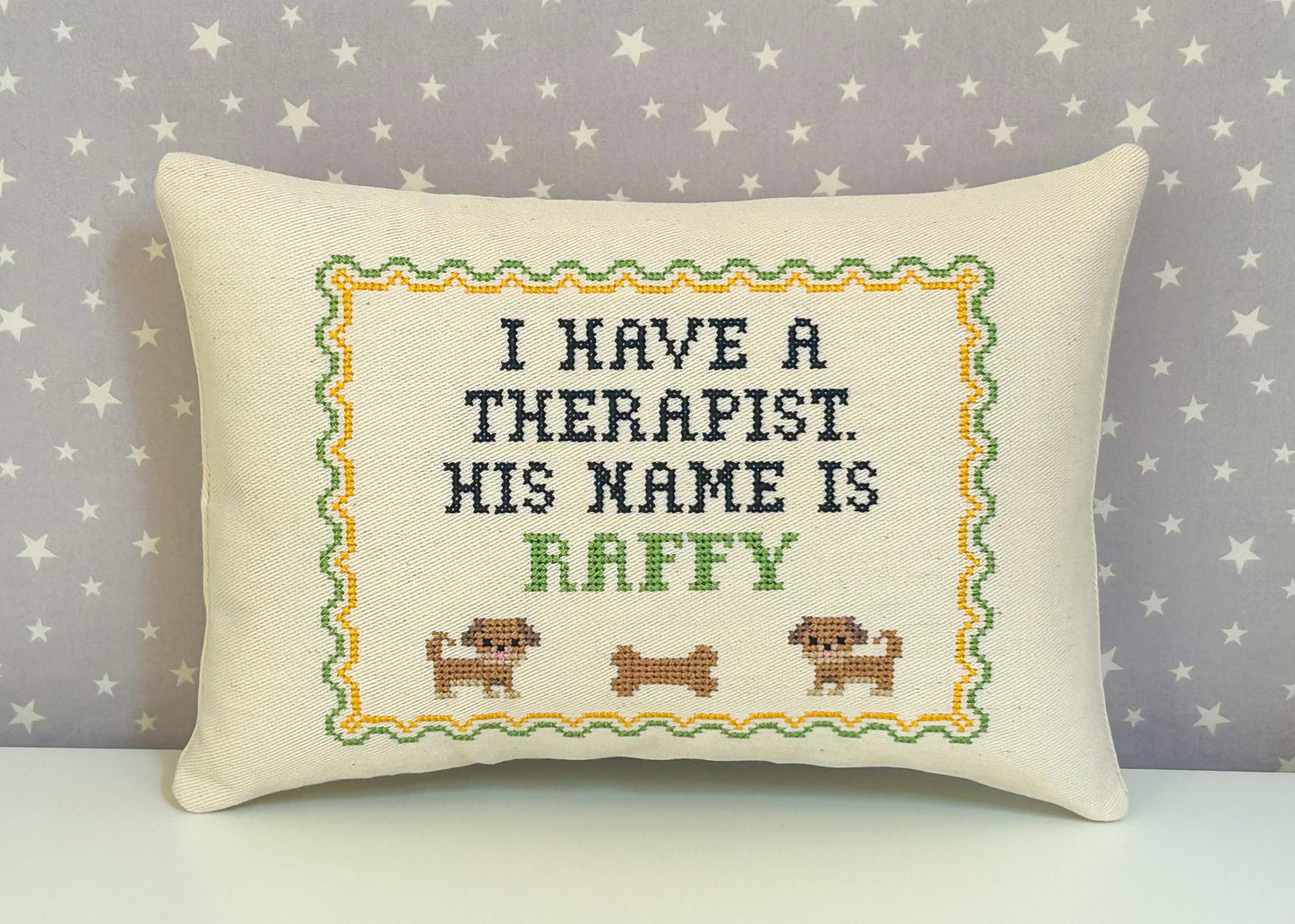 Decorative pillow with cross-stitched text and dog illustrations on a star-patterned background