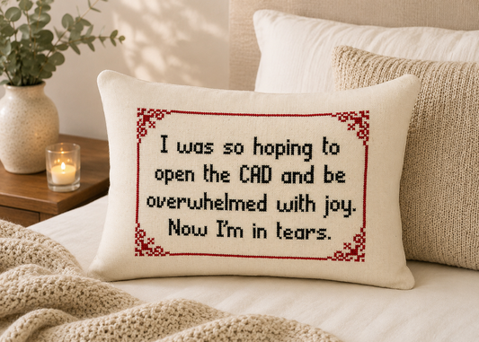 Decorative pillow with cross-stitched text on a couch, surrounded by pillows and a candle.