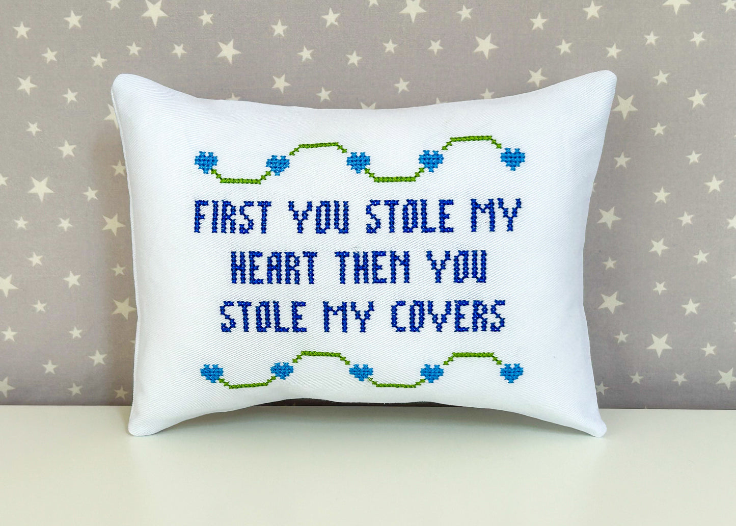 Decorative pillow with embroidered text and heart designs on a star-patterned background