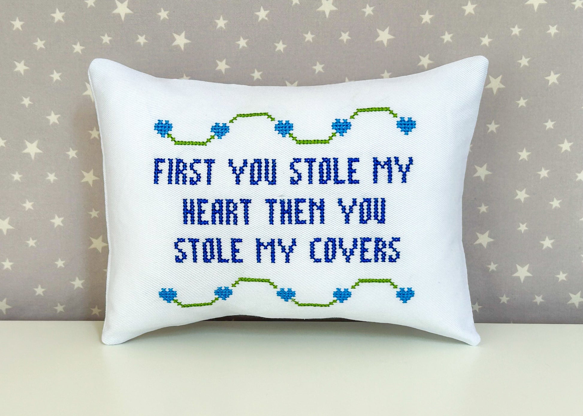 Decorative pillow with embroidered text and heart designs on a star-patterned background