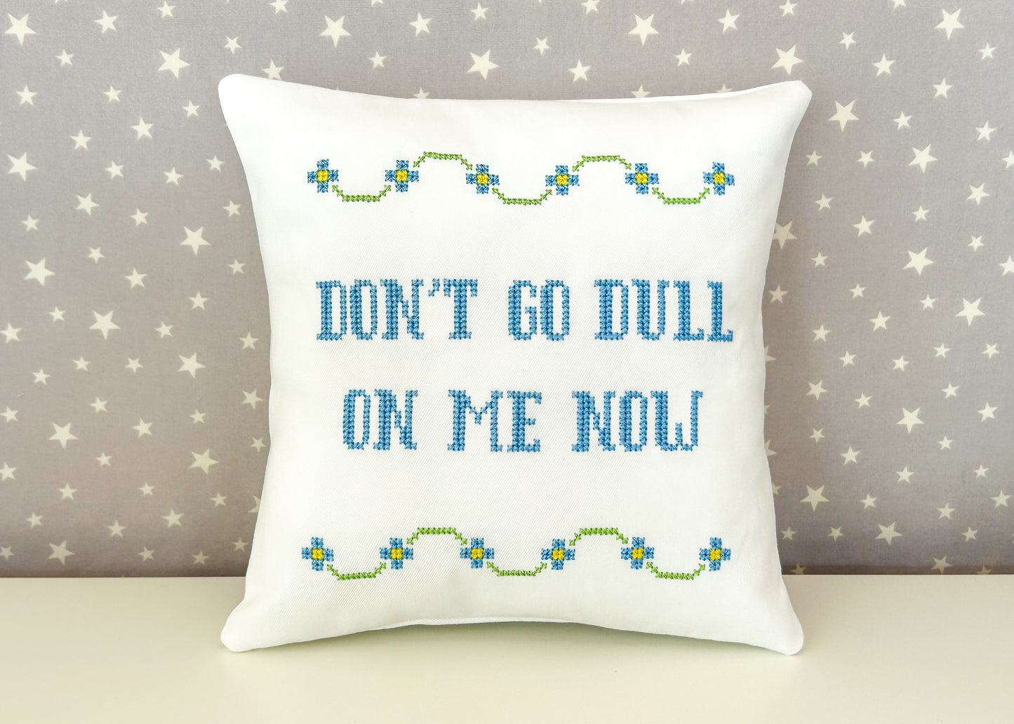 Decorative pillow with embroidered text and patterns on a star-patterned background