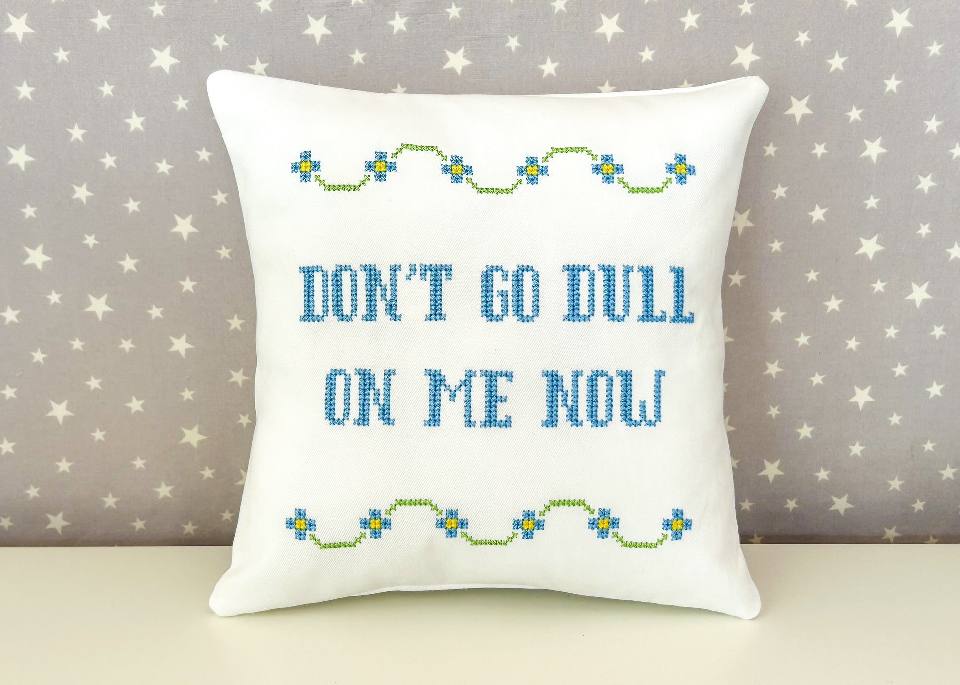 Decorative pillow with embroidered text and patterns on a star-patterned background