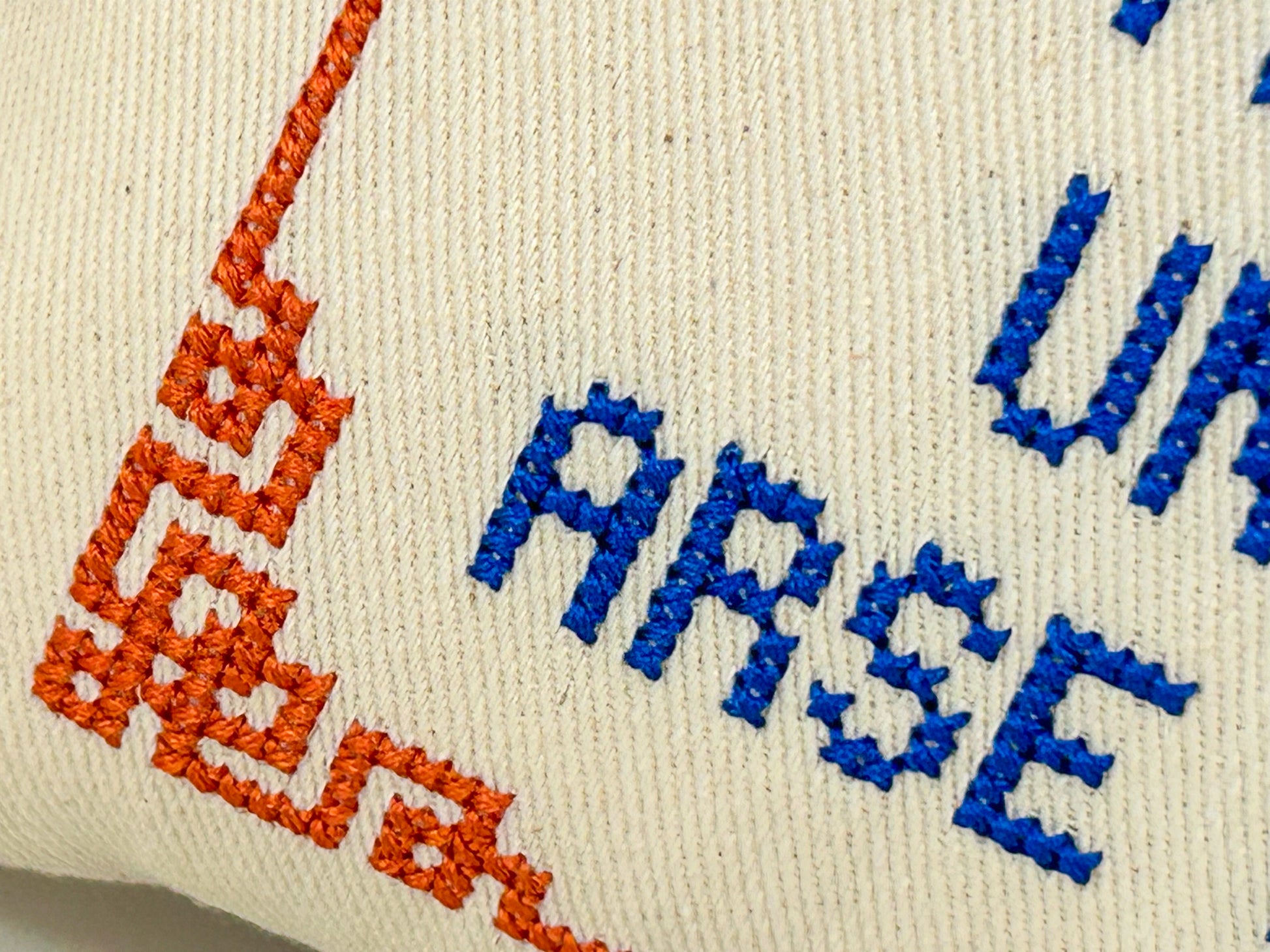 Embroidered text on a fabric with orange and blue thread.