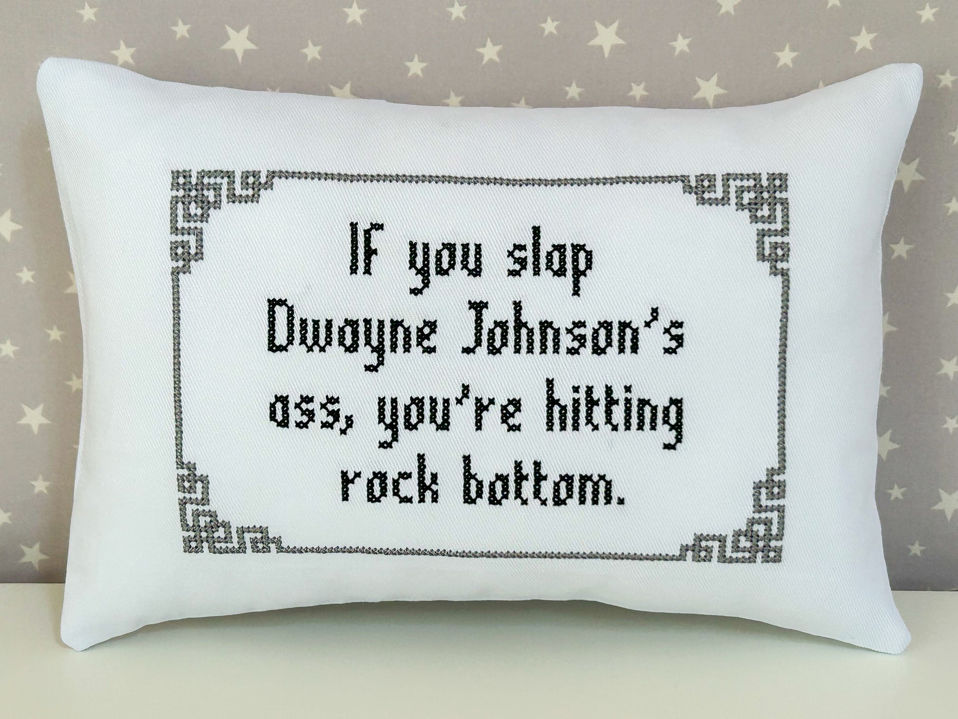 Decorative pillow with cross-stitched text on a neutral background