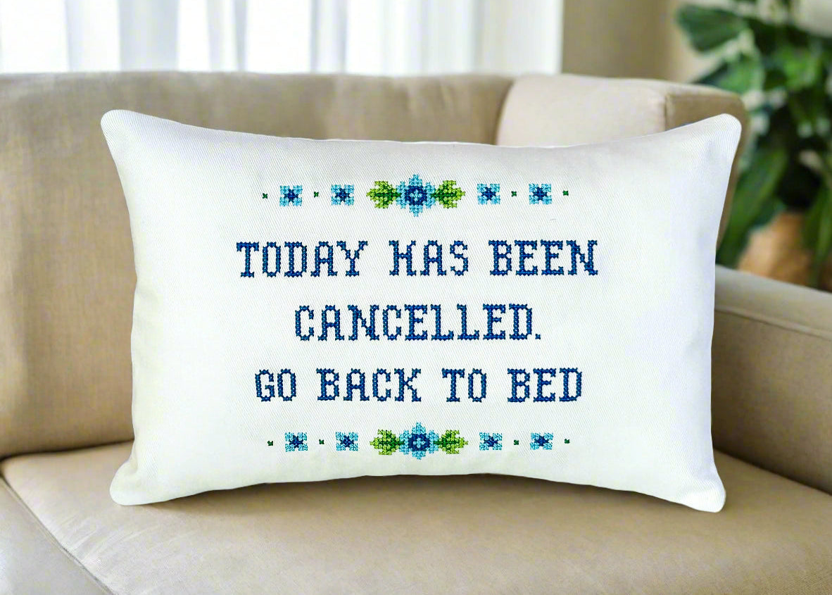 Decorative pillow with text 'Today has been cancelled. Go back to bed' on a beige couch.