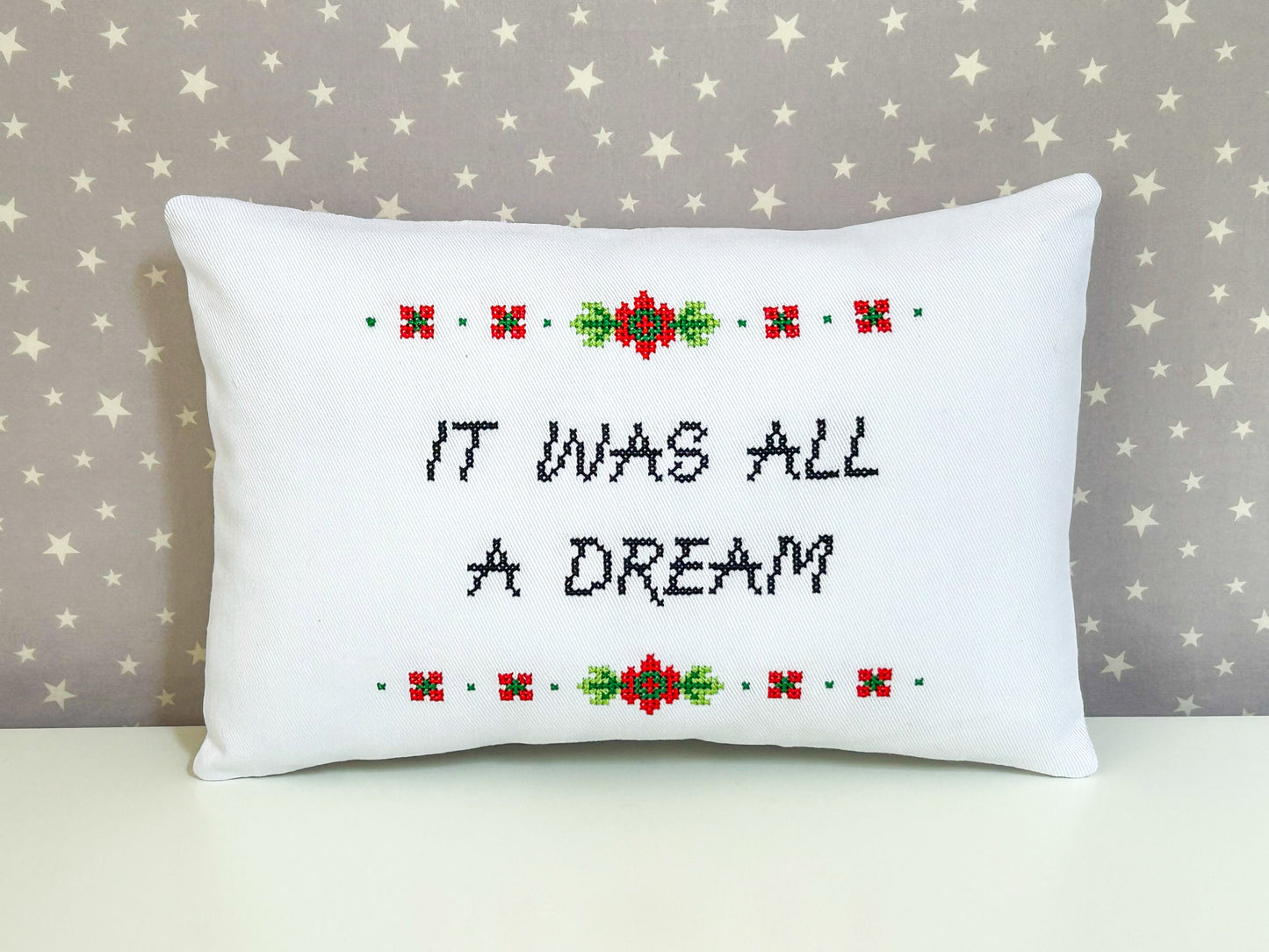 Decorative pillow with cross-stitched text and floral patterns on a star-patterned background