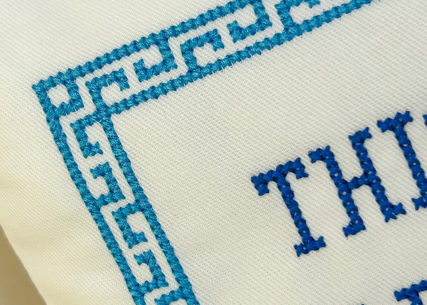 Text 'THIS' embroidered in blue on a white fabric background