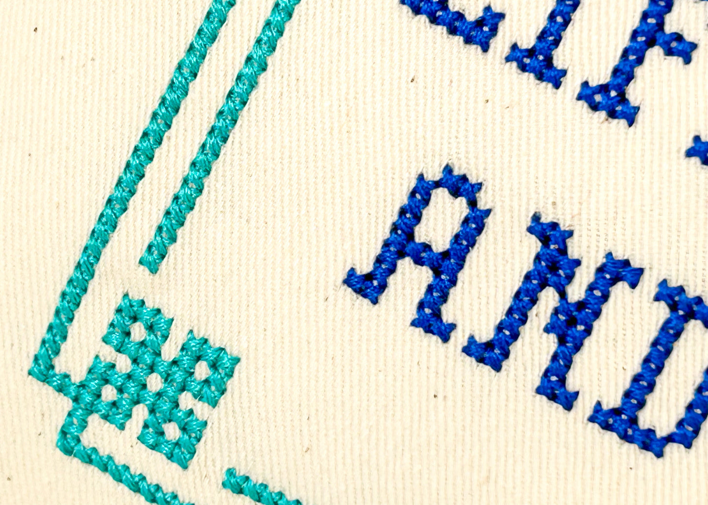 Embroidered text with blue and green thread on a beige fabric background