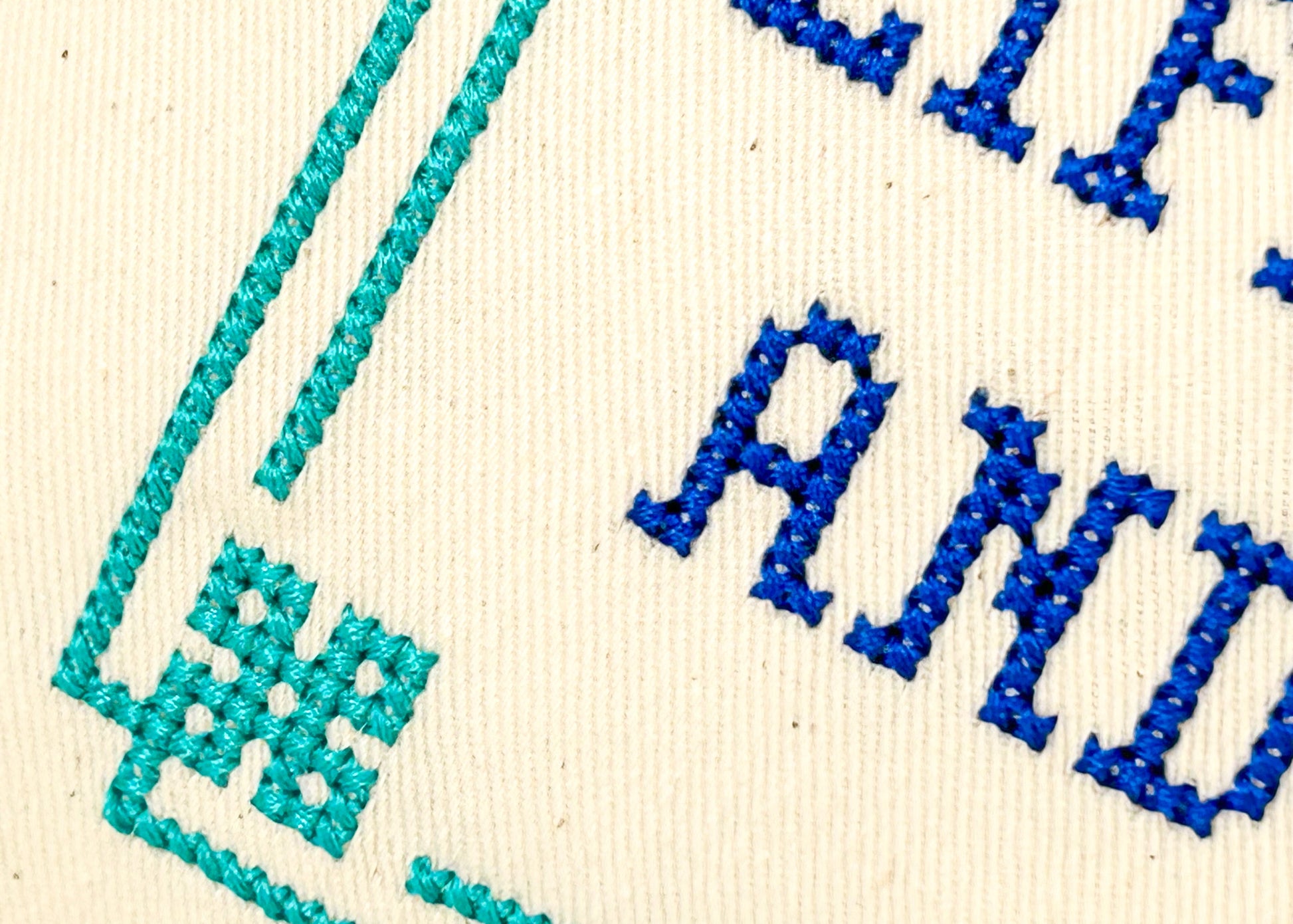 Embroidered text with blue and green thread on a beige fabric background
