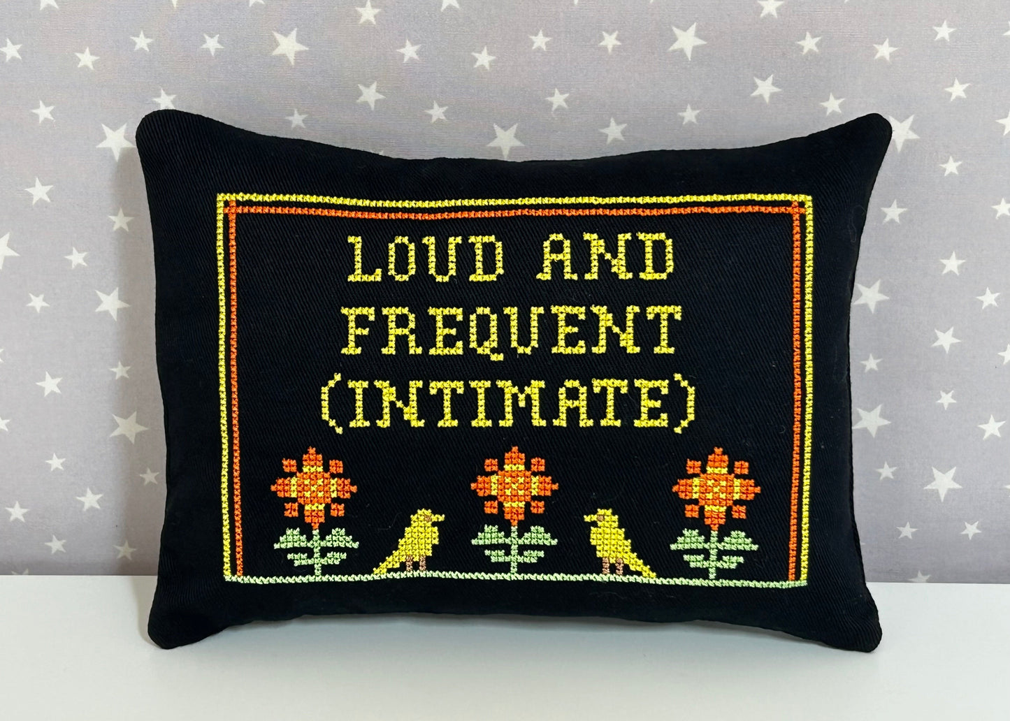 Decorative pillow with embroidered text and patterns on a star-patterned background