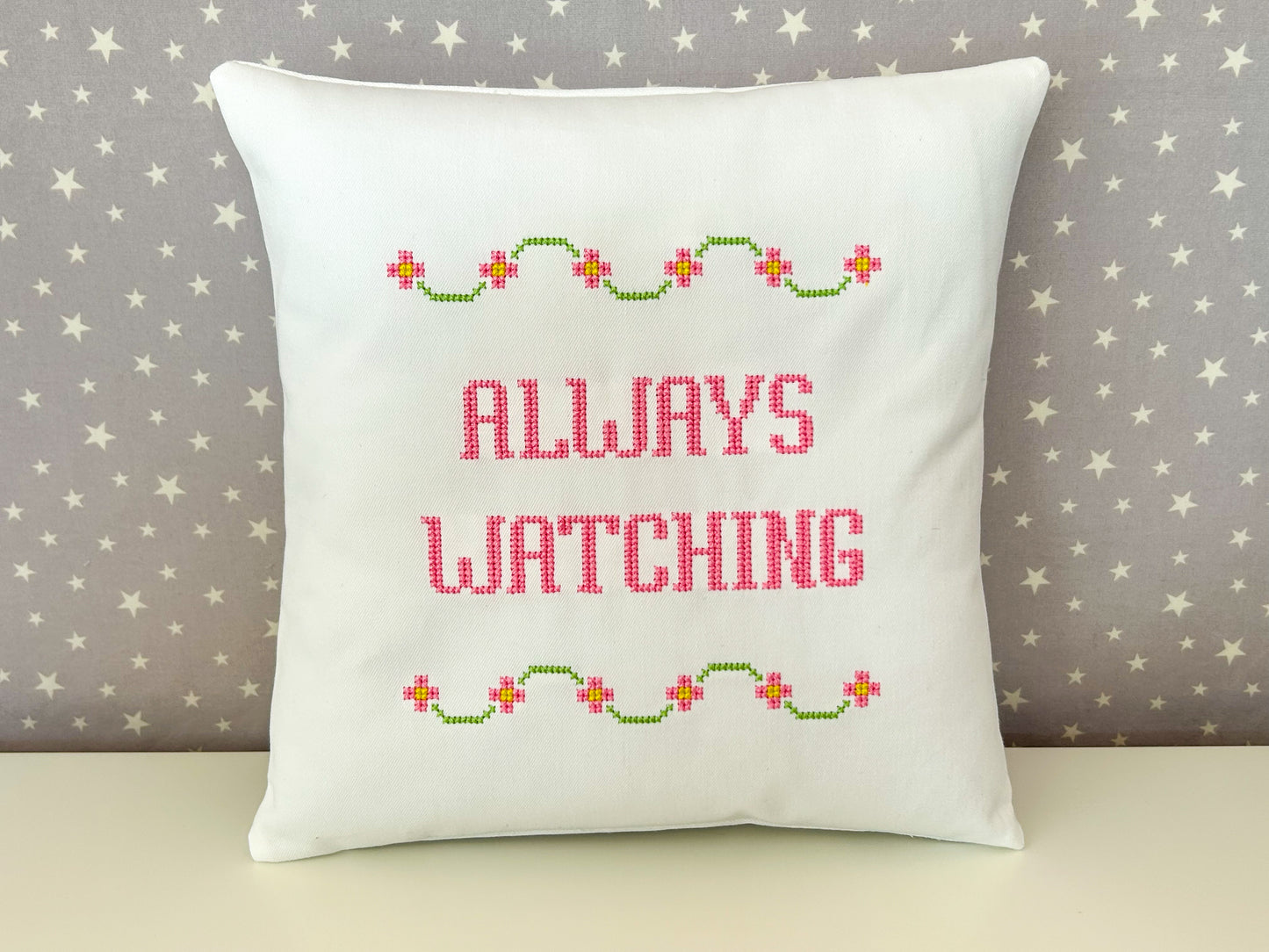 Decorative pillow with 'Always Watching' text and floral patterns on a star-patterned background