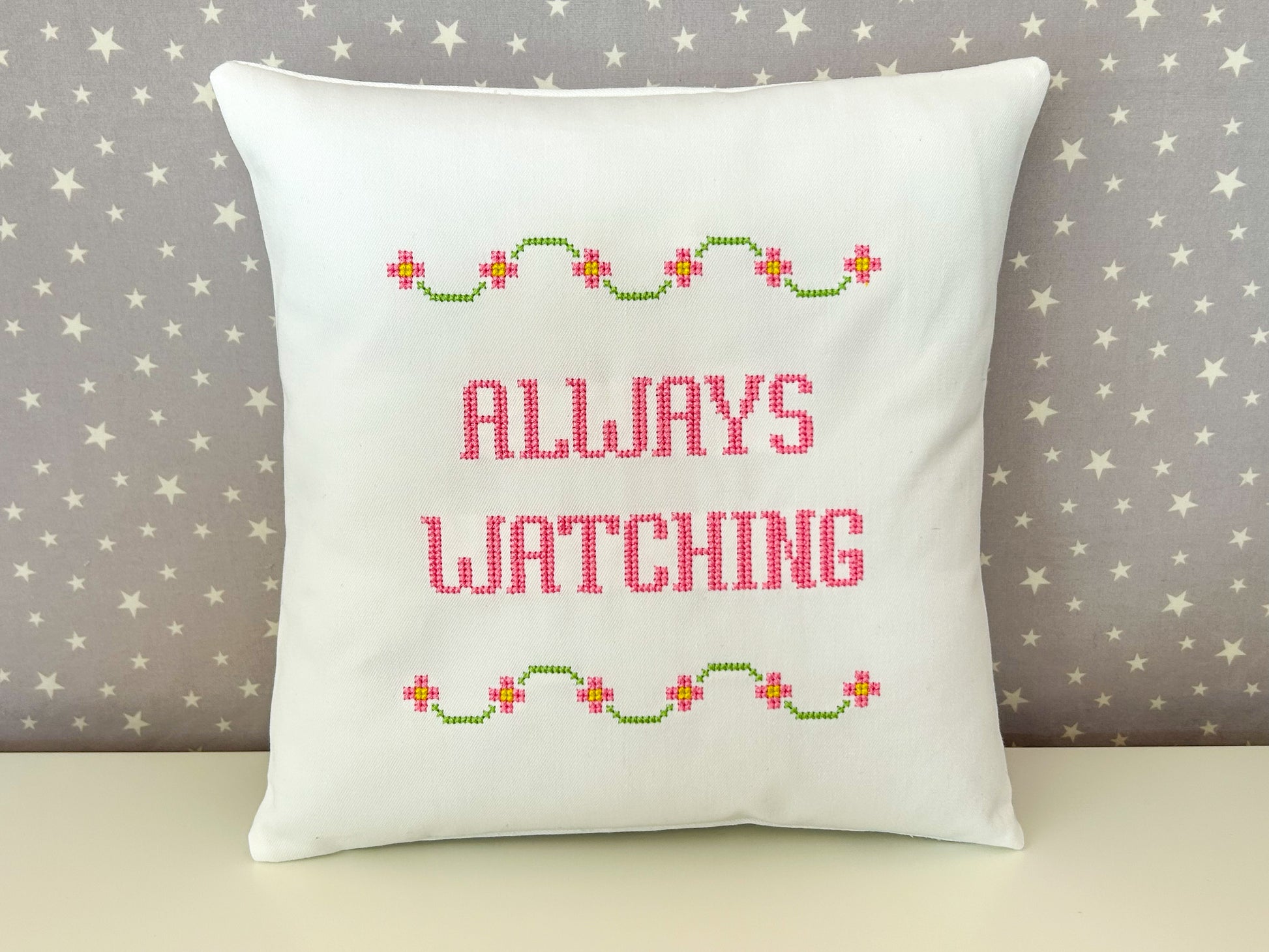 Decorative pillow with 'Always Watching' text and floral patterns on a star-patterned background