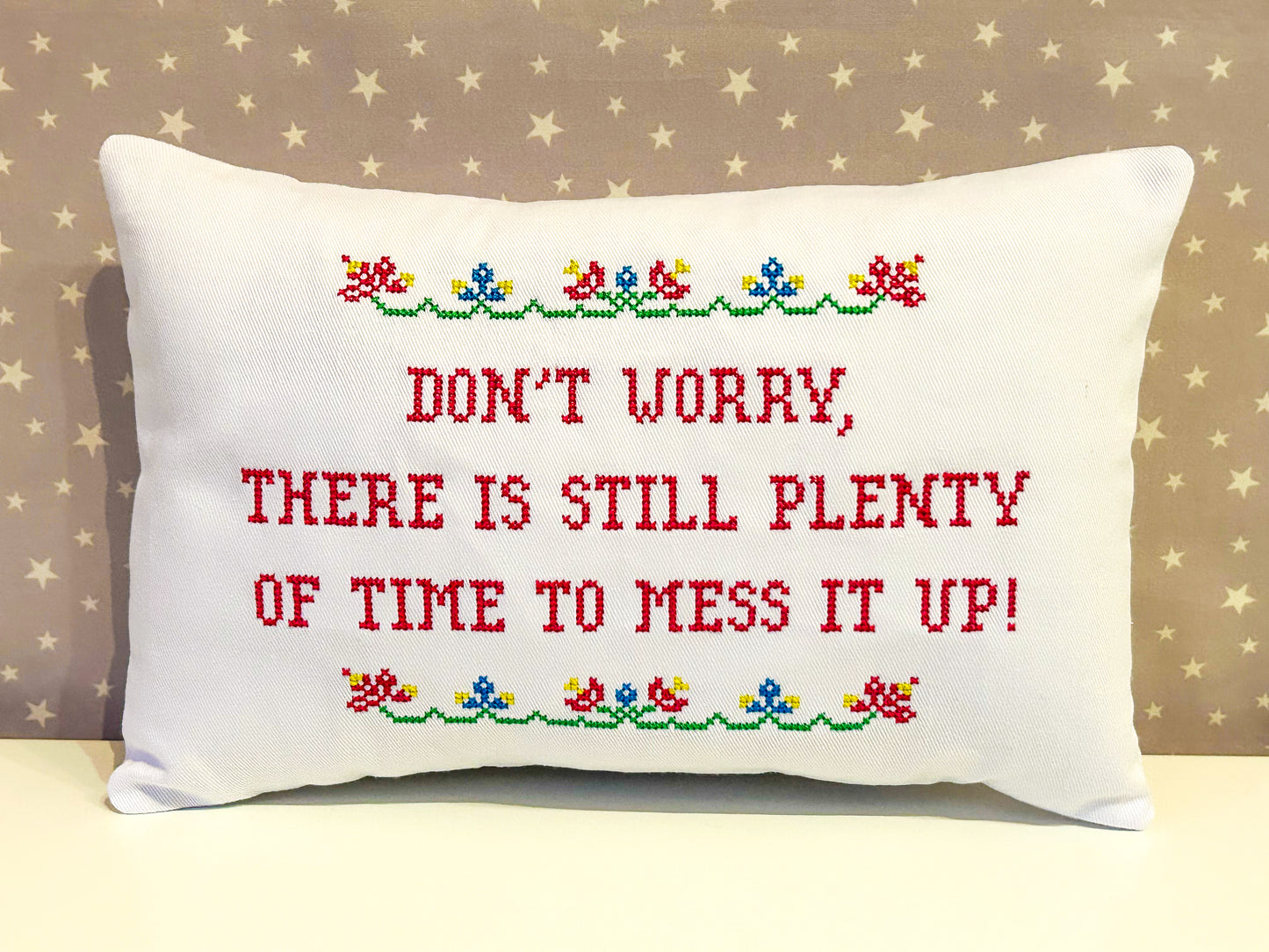 Decorative pillow with embroidered text and floral patterns on a beige background