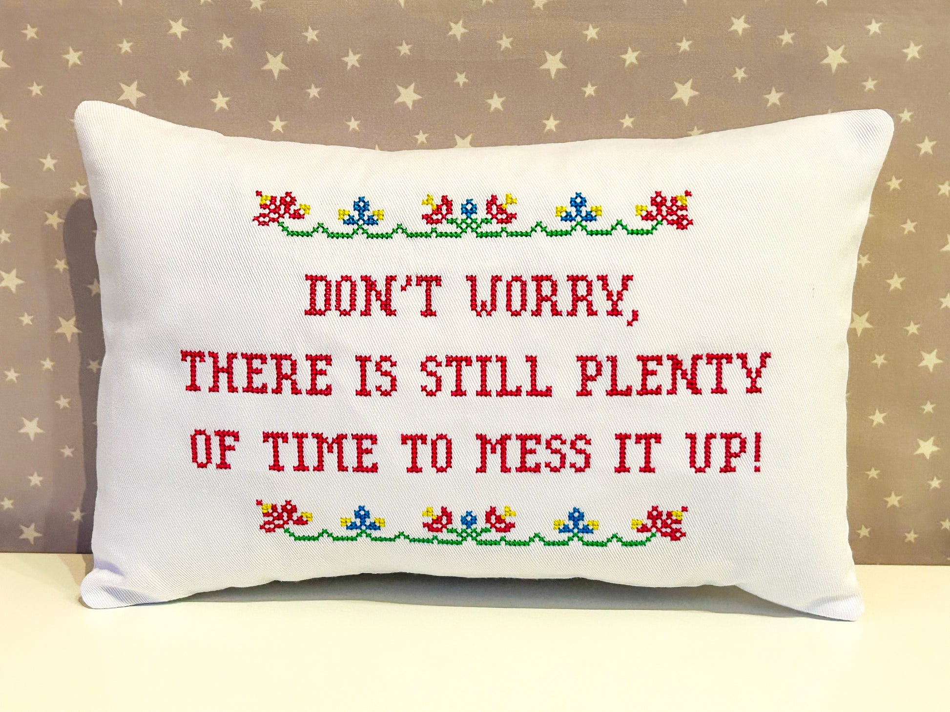 Decorative pillow with embroidered text and floral patterns on a beige background