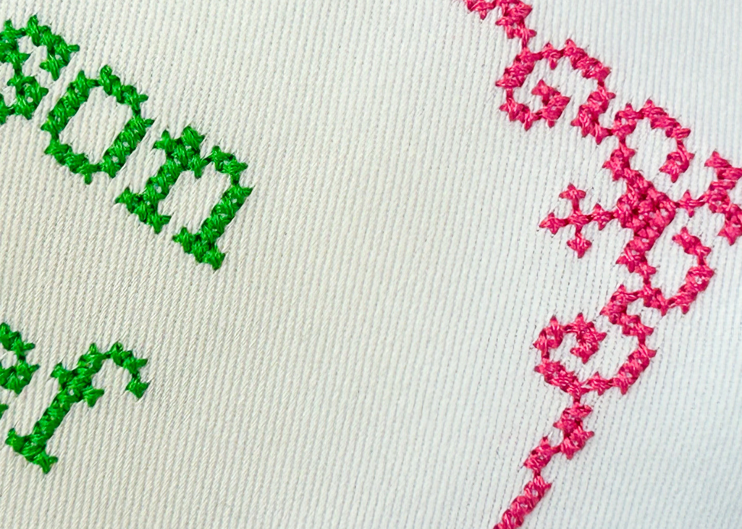 Embroidery with green text and pink pattern on a white fabric background