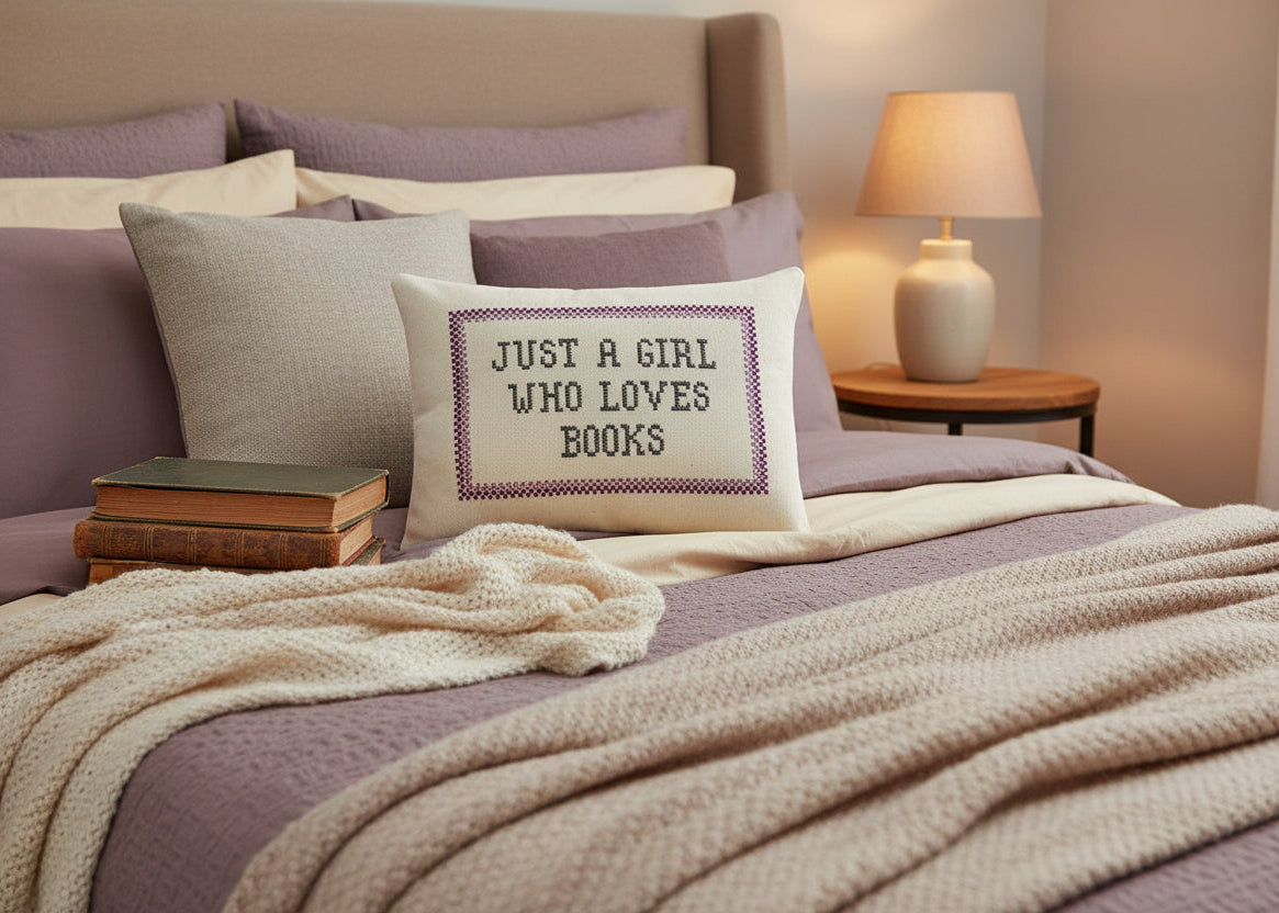 Bedroom with a pillow that says 'Just a girl who loves books' and a lamp on a nightstand.