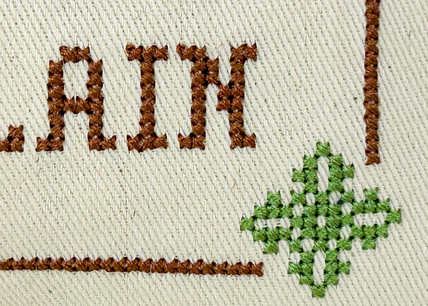 Embroidery with the word 'RAIN' and a green cross on beige fabric