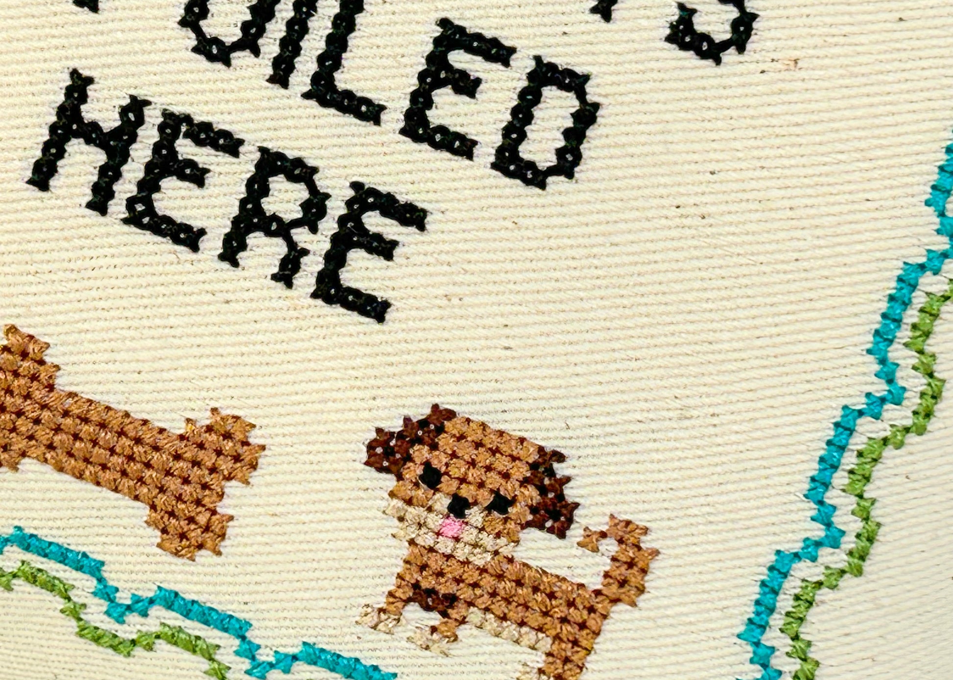 Cross-stitched design with a dog and text on beige fabric