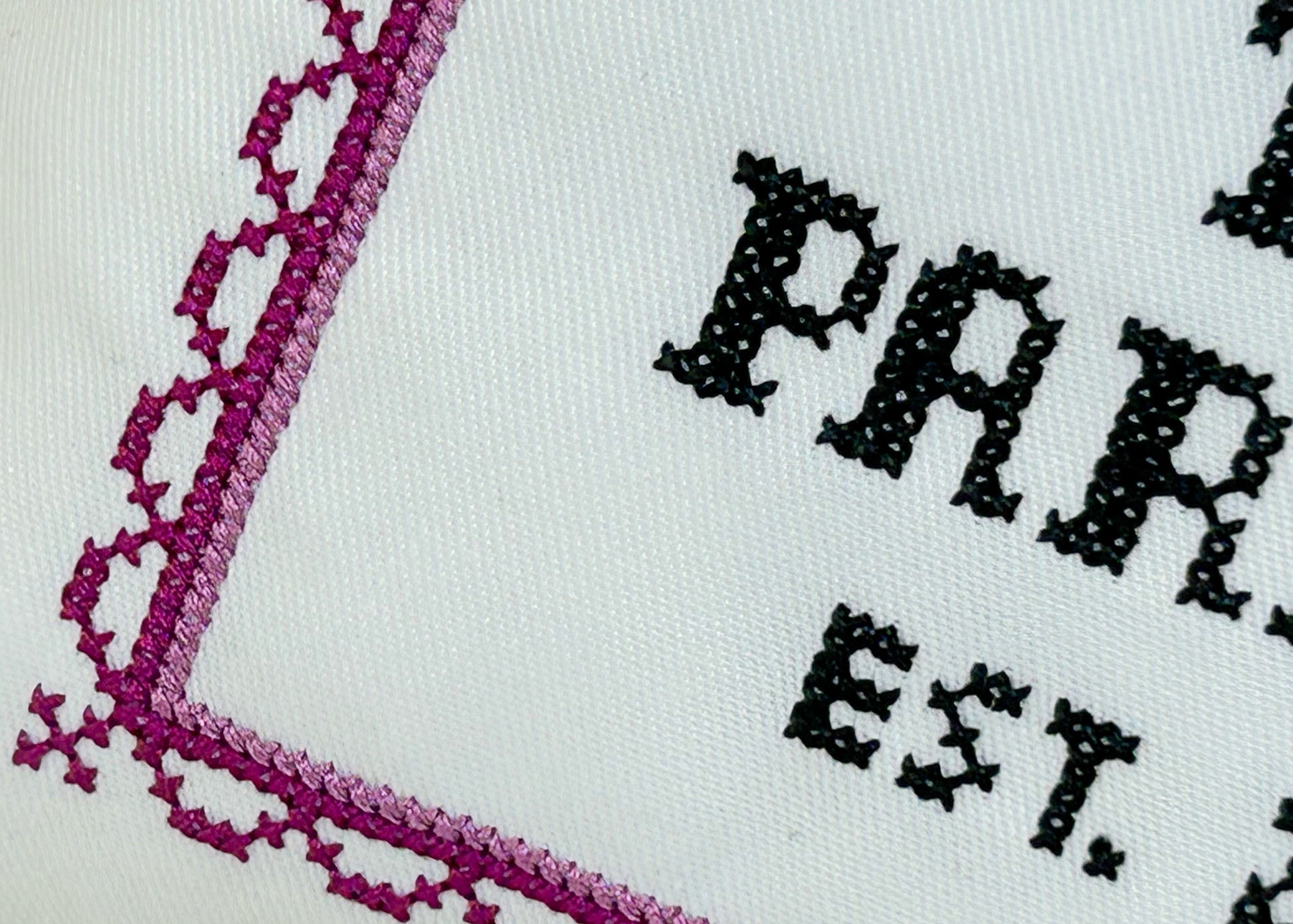 Embroidered text 'PARIS EST.' on a white fabric with pink lace trim.