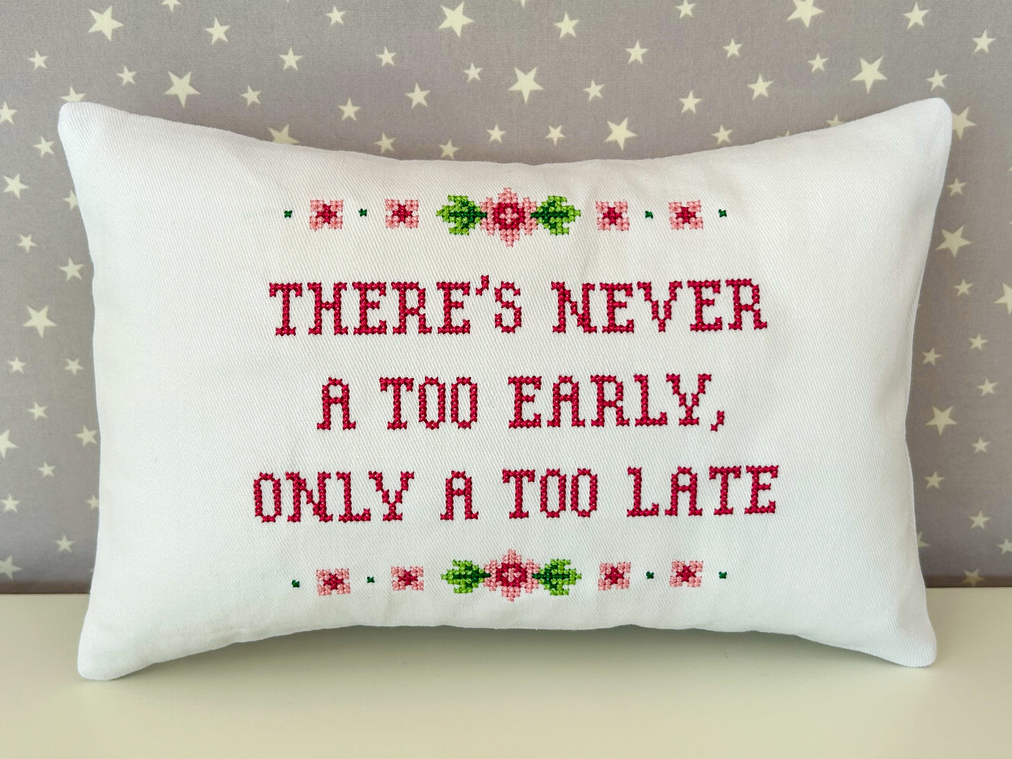 Decorative pillow with cross-stitched text and floral patterns on a star-patterned background