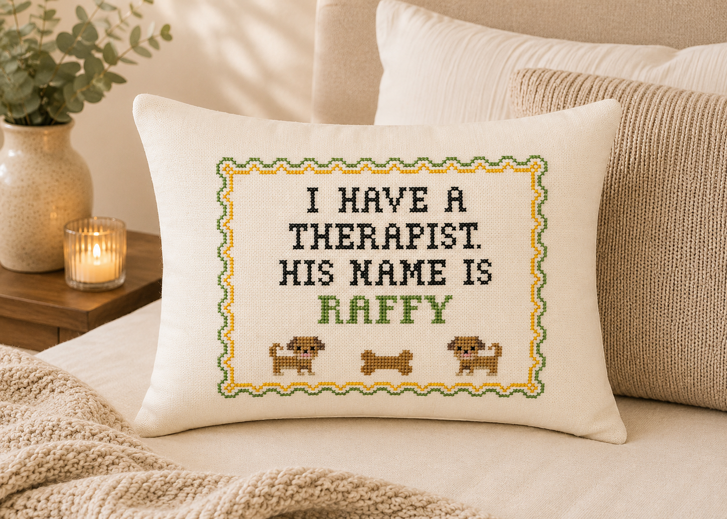 Decorative pillow with cross-stitched text on a couch, surrounded by pillows and a candle.