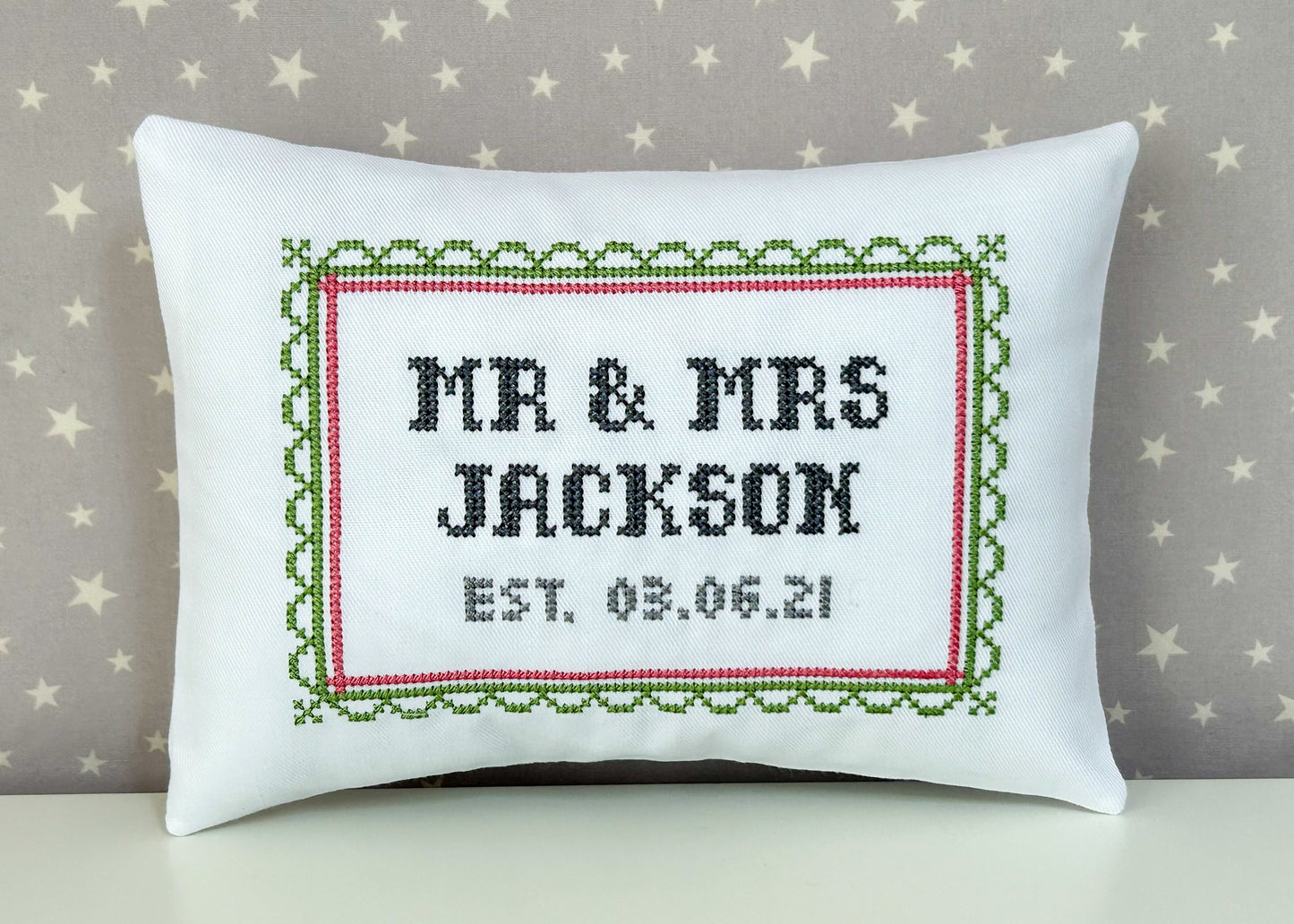 Decorative pillow with cross-stitched text 'MR & MRS JACKSON EST. 03.06.21' on a star-patterned background