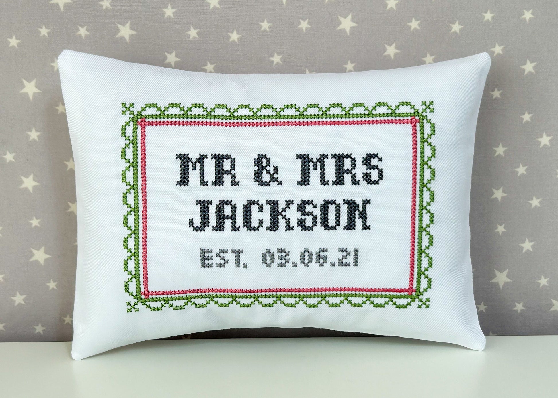 Decorative pillow with cross-stitched text 'MR & MRS JACKSON EST. 03.06.21' on a star-patterned background