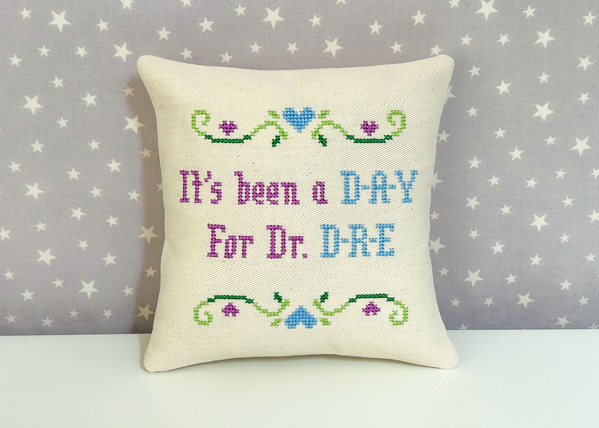Decorative pillow with cross-stitched text on a star-patterned background