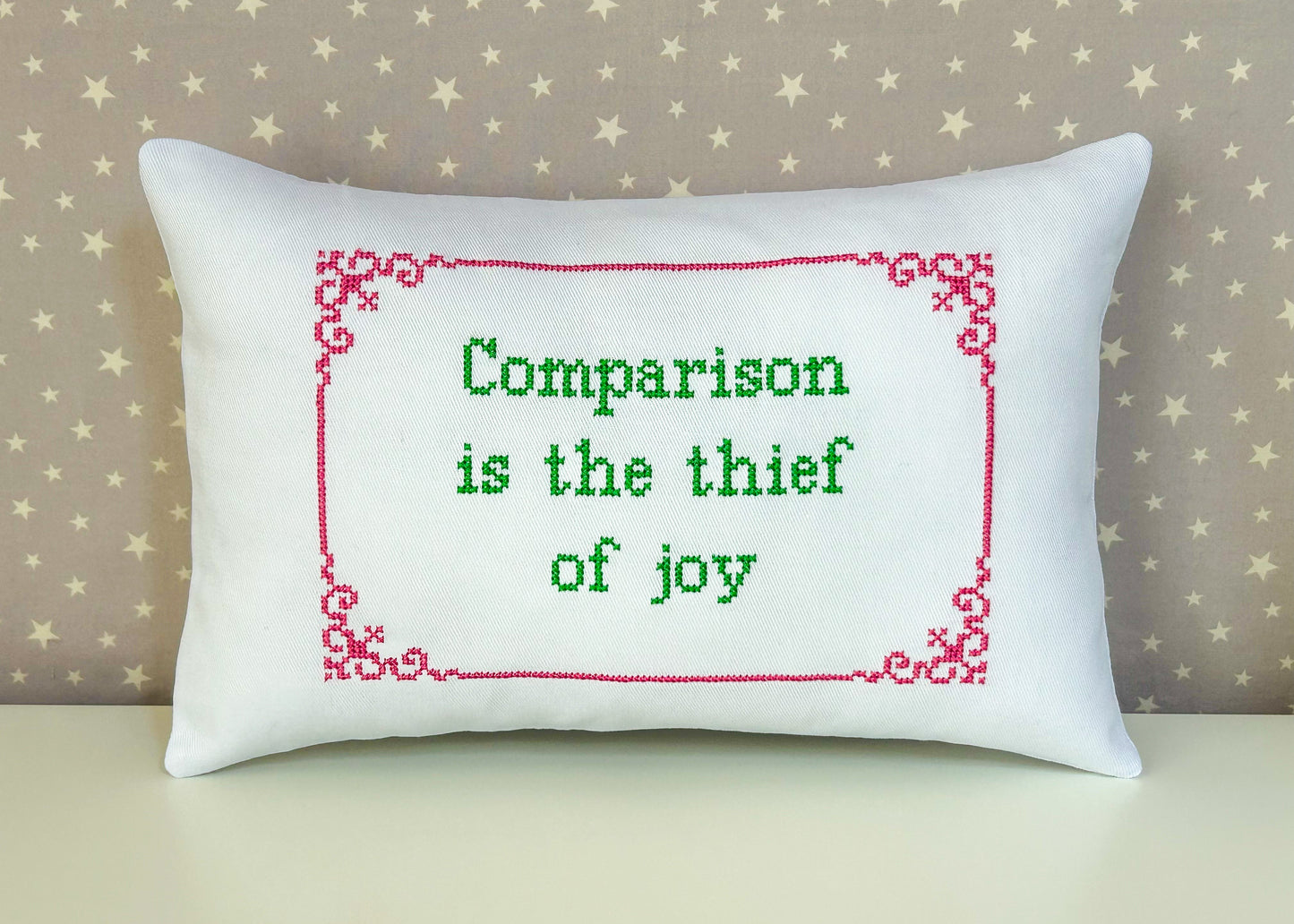 Decorative pillow with embroidered message 'Comparison is the thief of joy' on a star-patterned background.