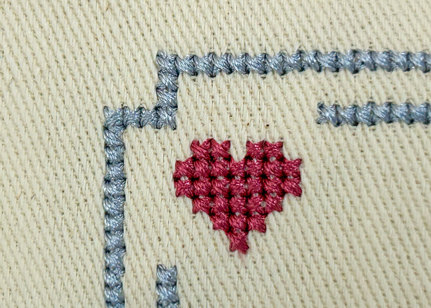 Embroidered red heart on beige fabric with gray stitching
