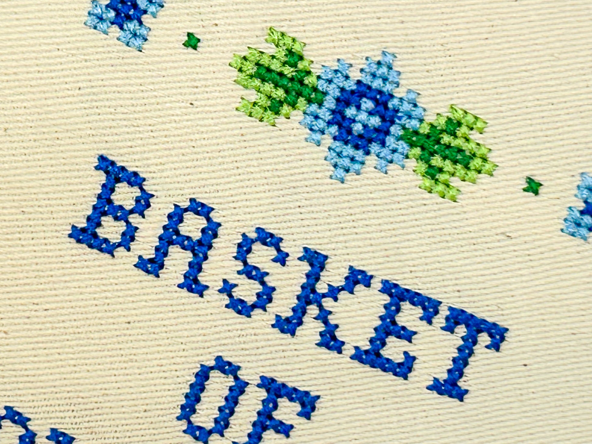 Cross-stitched text 'Basket of' with floral design on beige fabric