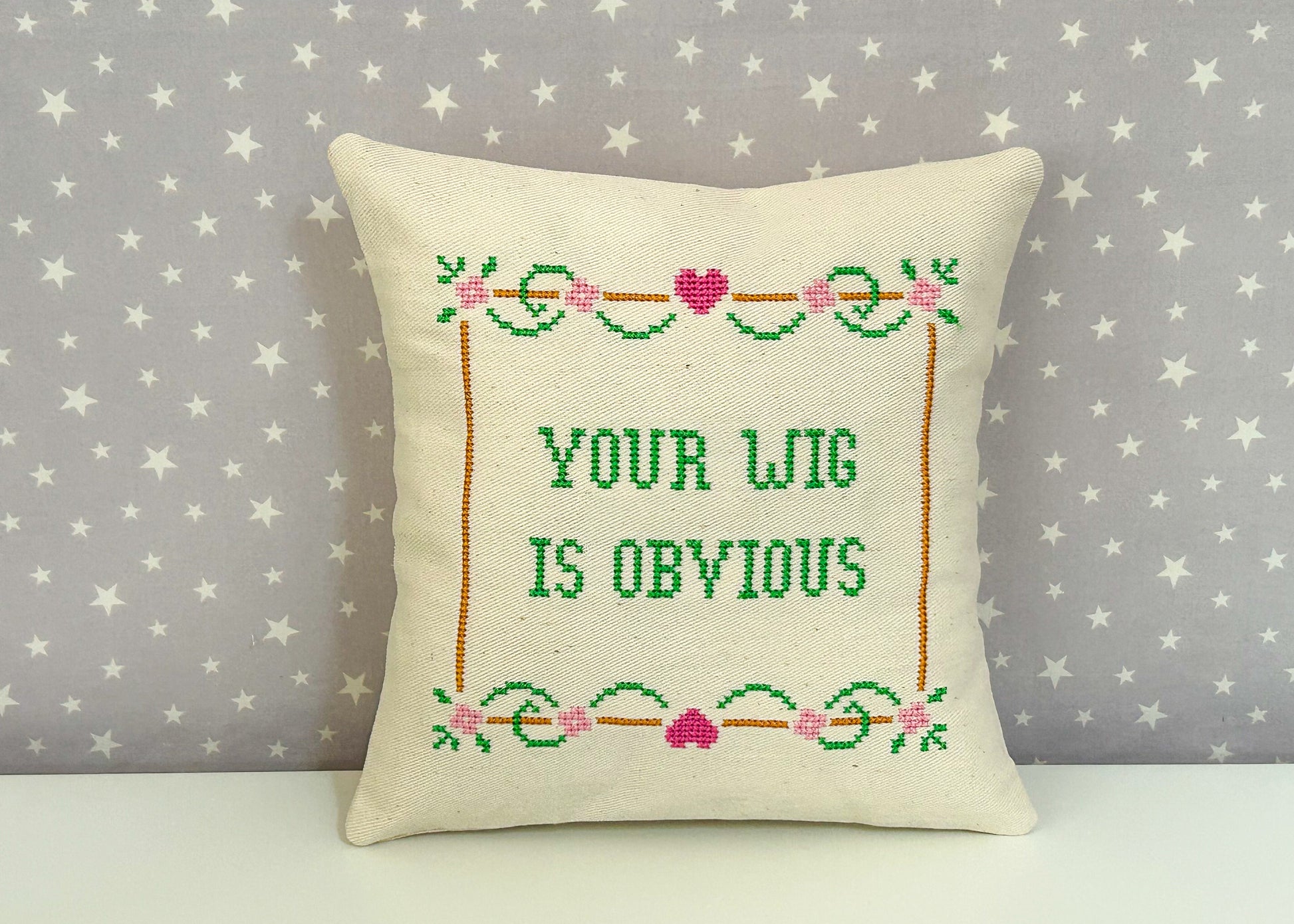 Decorative pillow with cross-stitched text on a star-patterned background