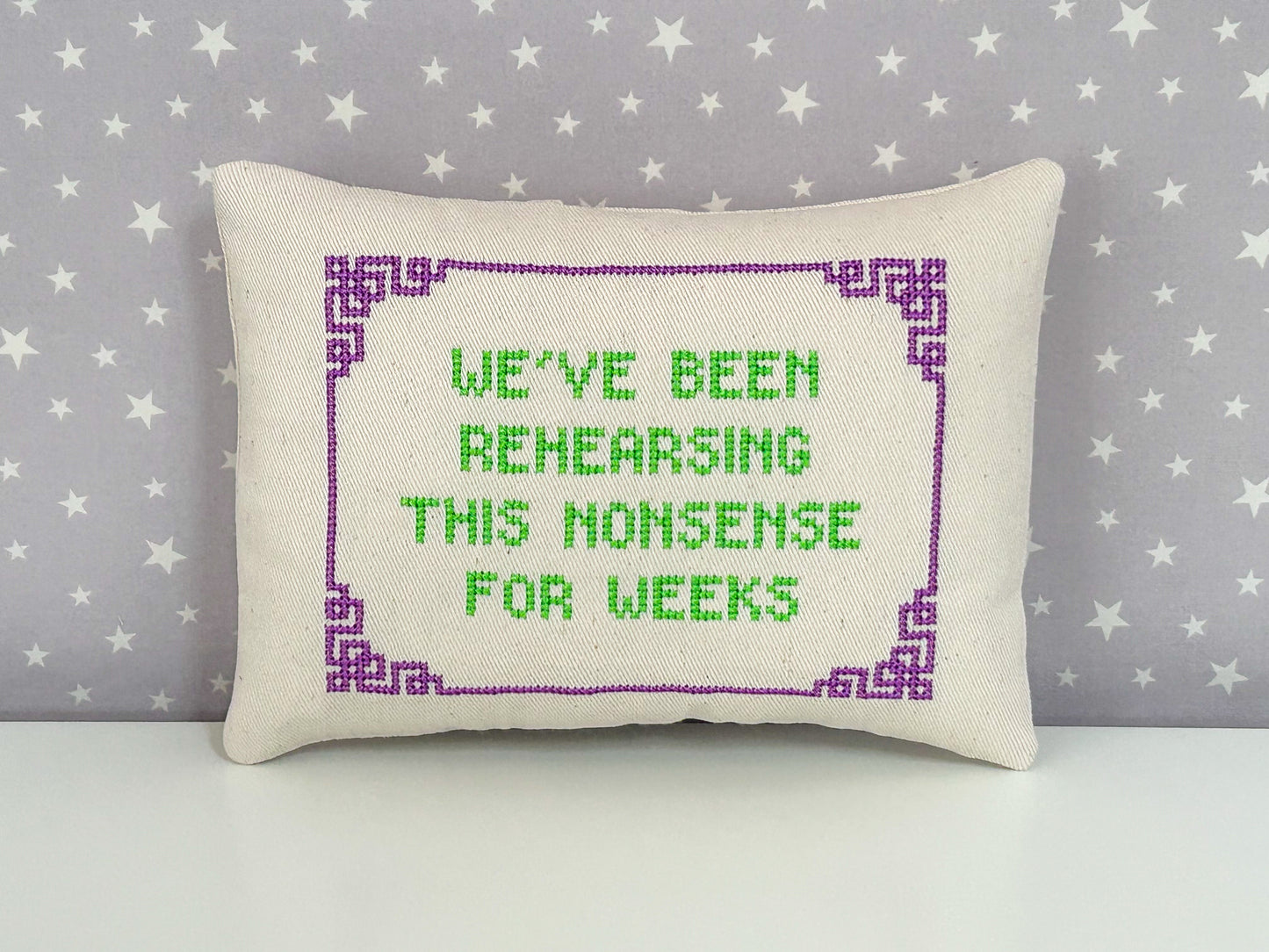 Decorative pillow with cross-stitched text on a star-patterned background