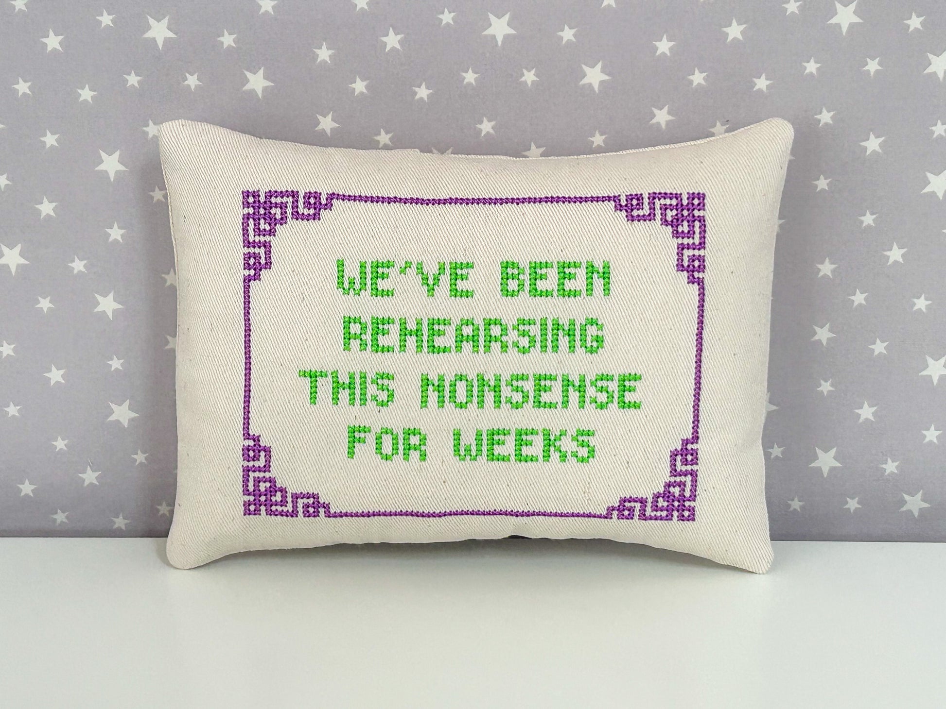 Decorative pillow with cross-stitched text on a star-patterned background