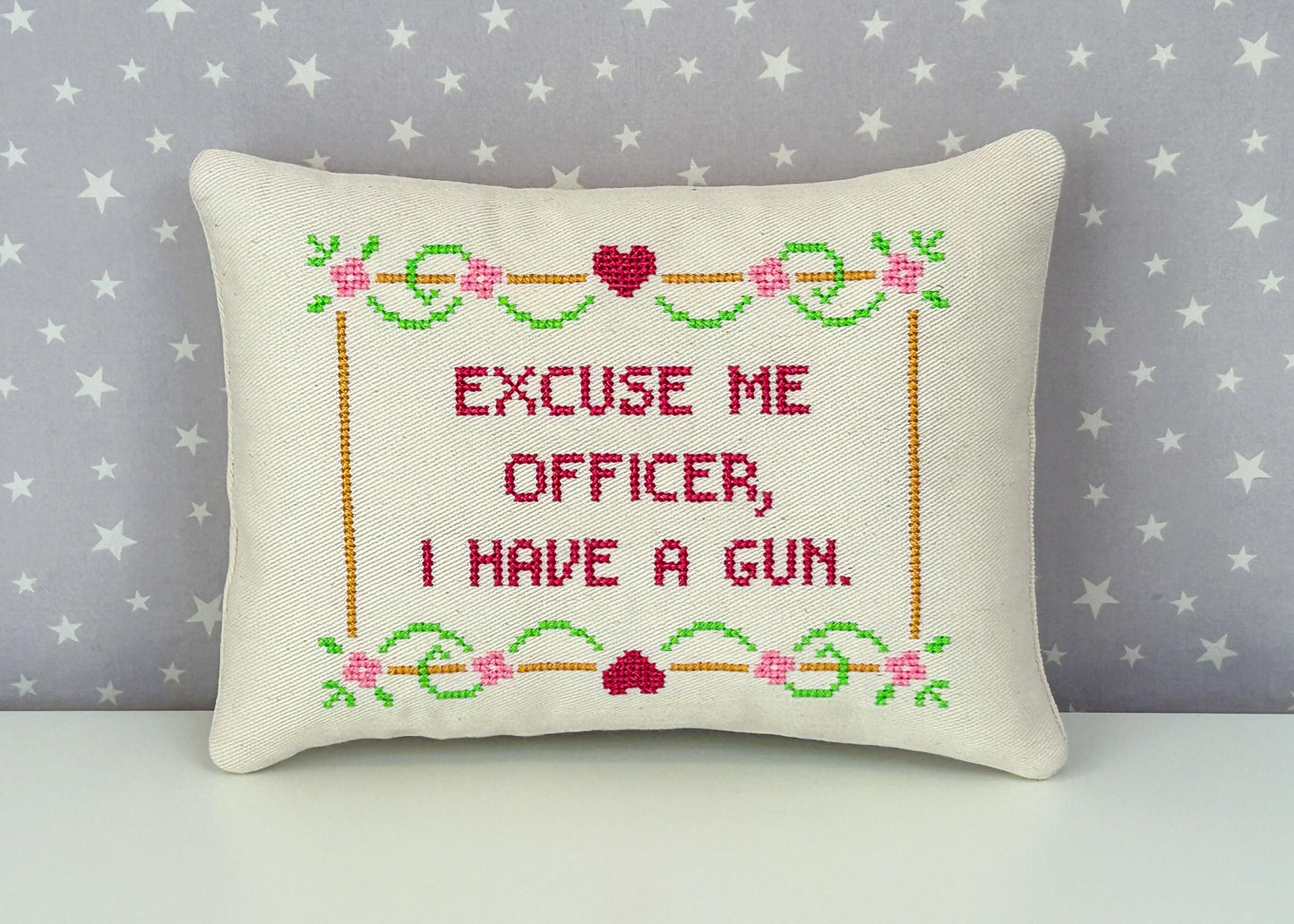 Decorative pillow with cross-stitched text and floral patterns on a star-patterned background