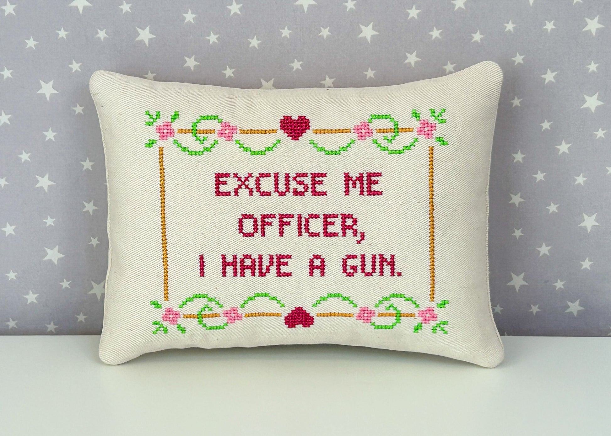 Decorative pillow with cross-stitched text and floral patterns on a star-patterned background