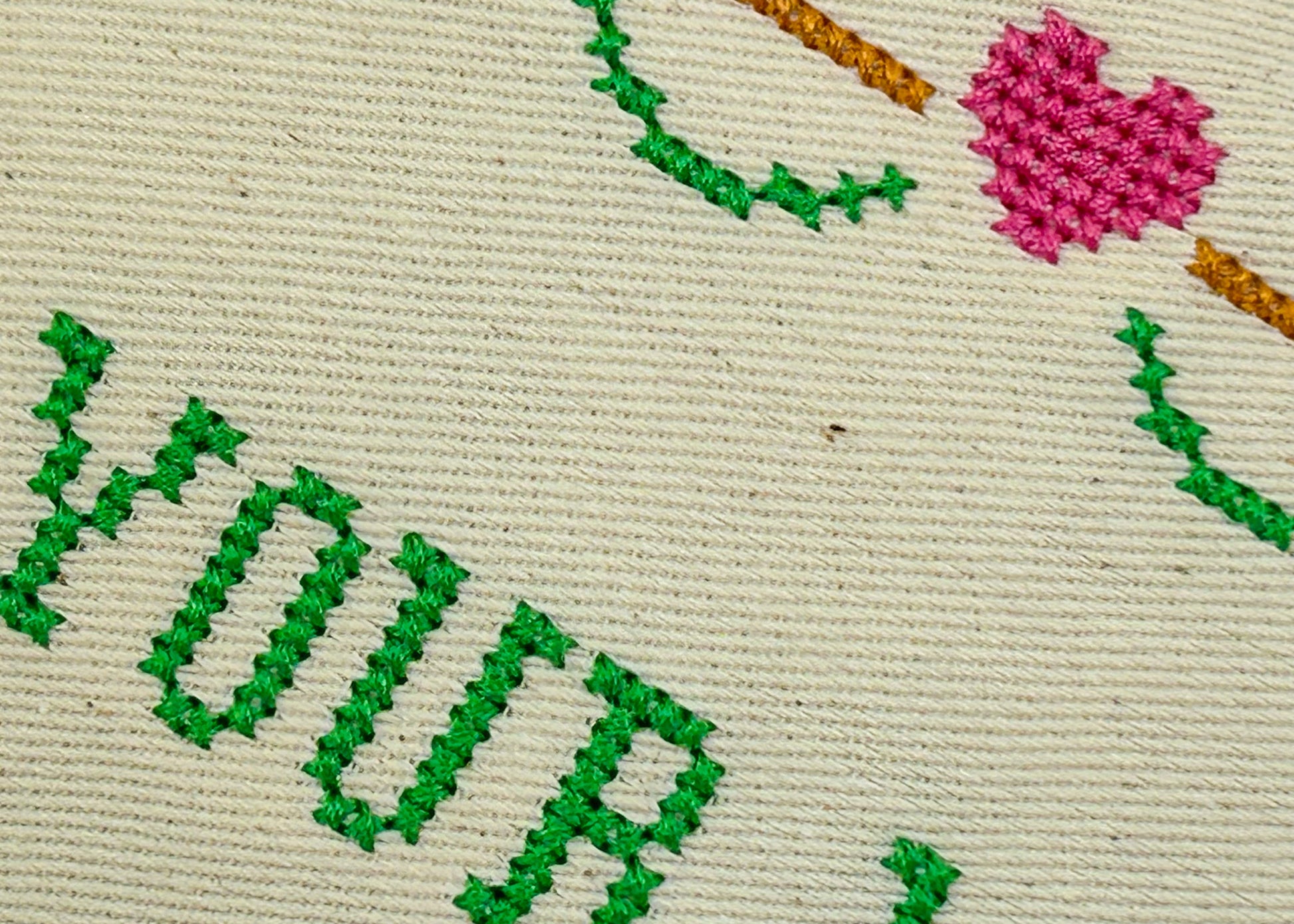Embroidery with green text and pink heart on beige fabric