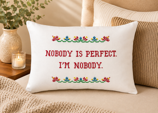 Decorative pillow with cross-stitched text on a couch, surrounded by pillows and a candle.