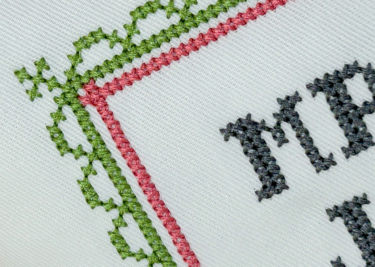 Embroidery with green and red border and black text on white fabric