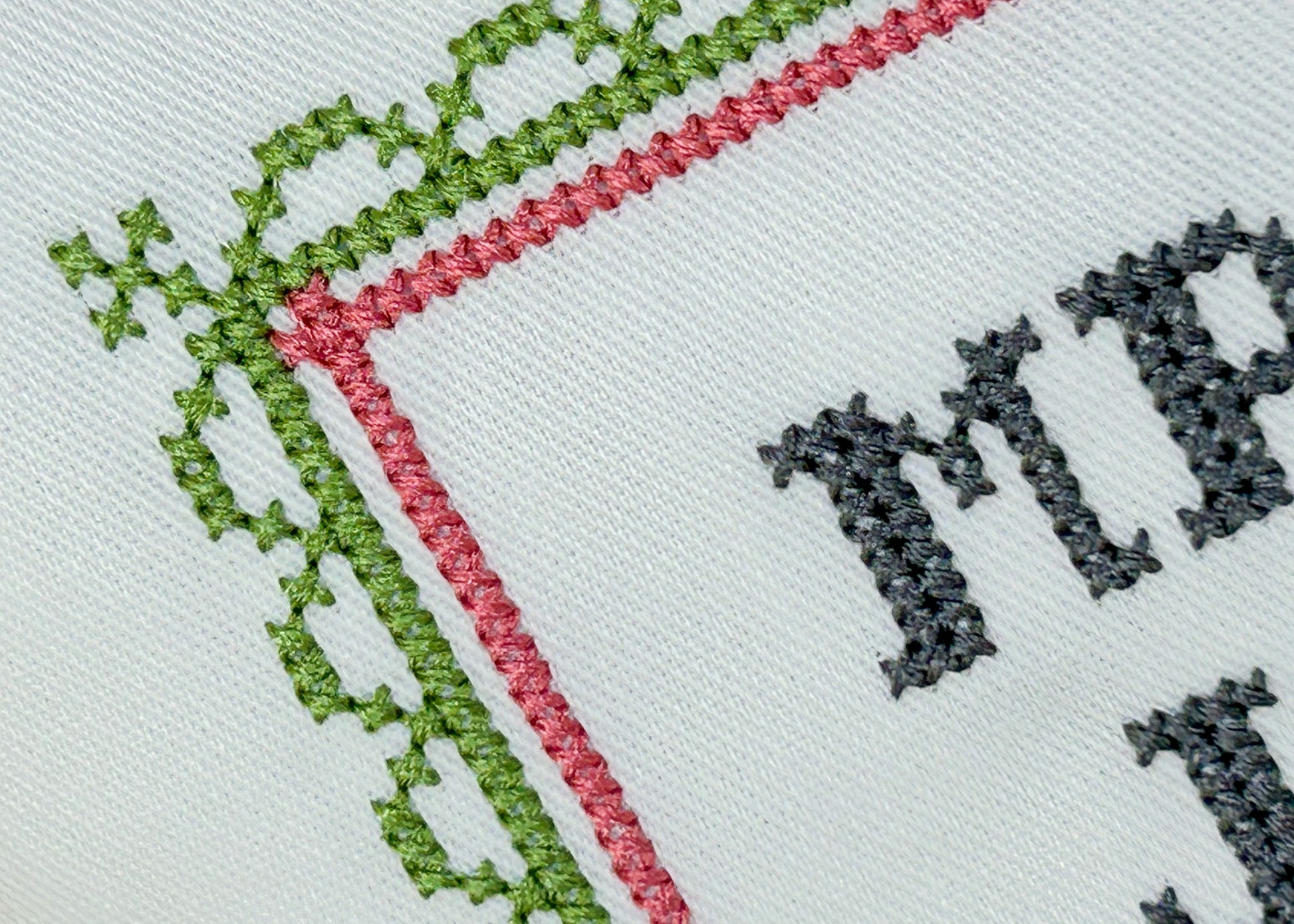 Embroidery with green and red border and black text on white fabric
