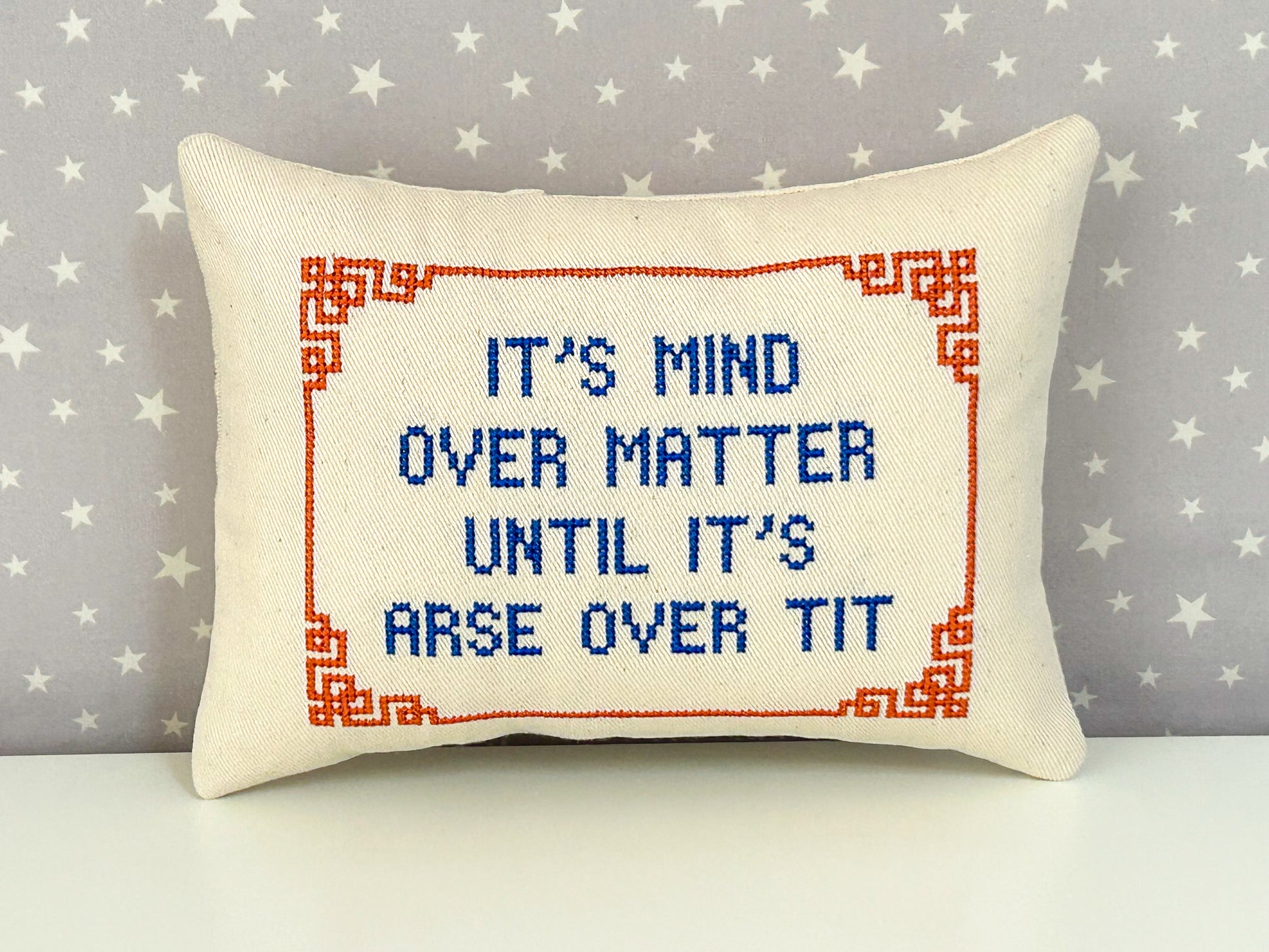 Decorative pillow with cross-stitched text on a star-patterned background