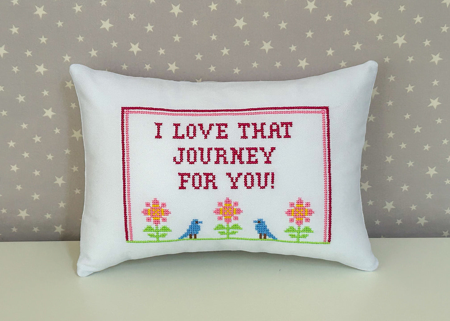 Decorative pillow with embroidered text and flowers on a star-patterned background