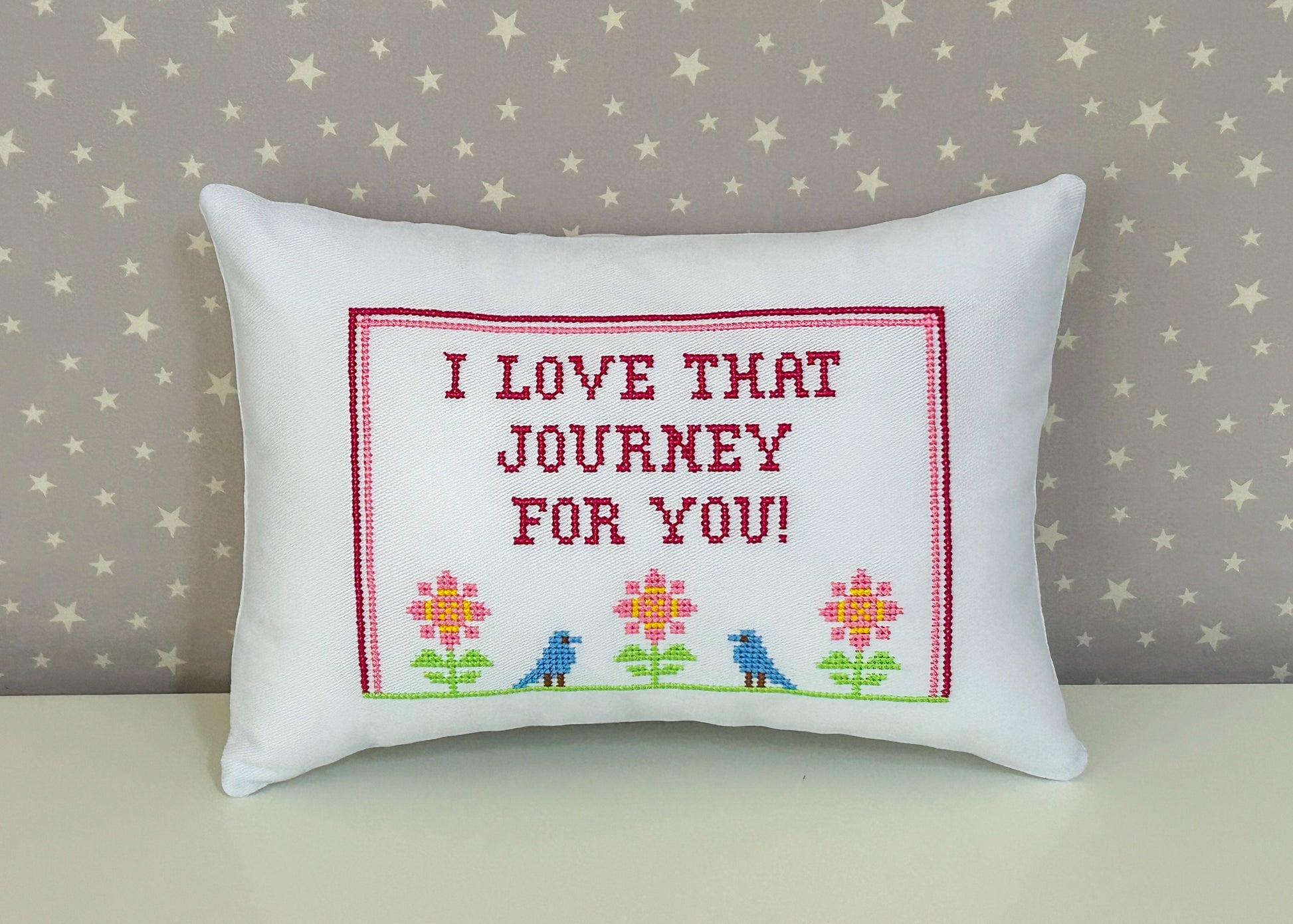 Decorative pillow with embroidered text and flowers on a star-patterned background
