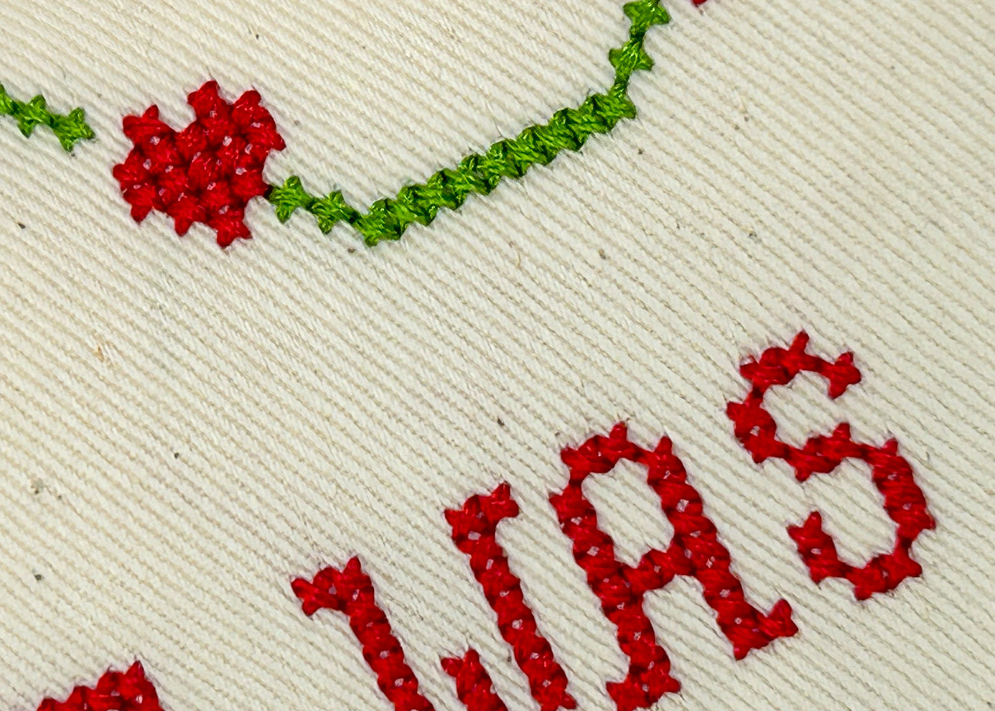 Cross-stitched text with red letters and green thread on beige fabric