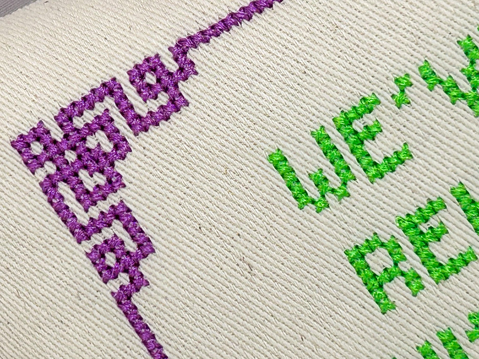 Embroidered text with 'HELLO' in purple and 'WE LOVE' in green on a textured fabric background.